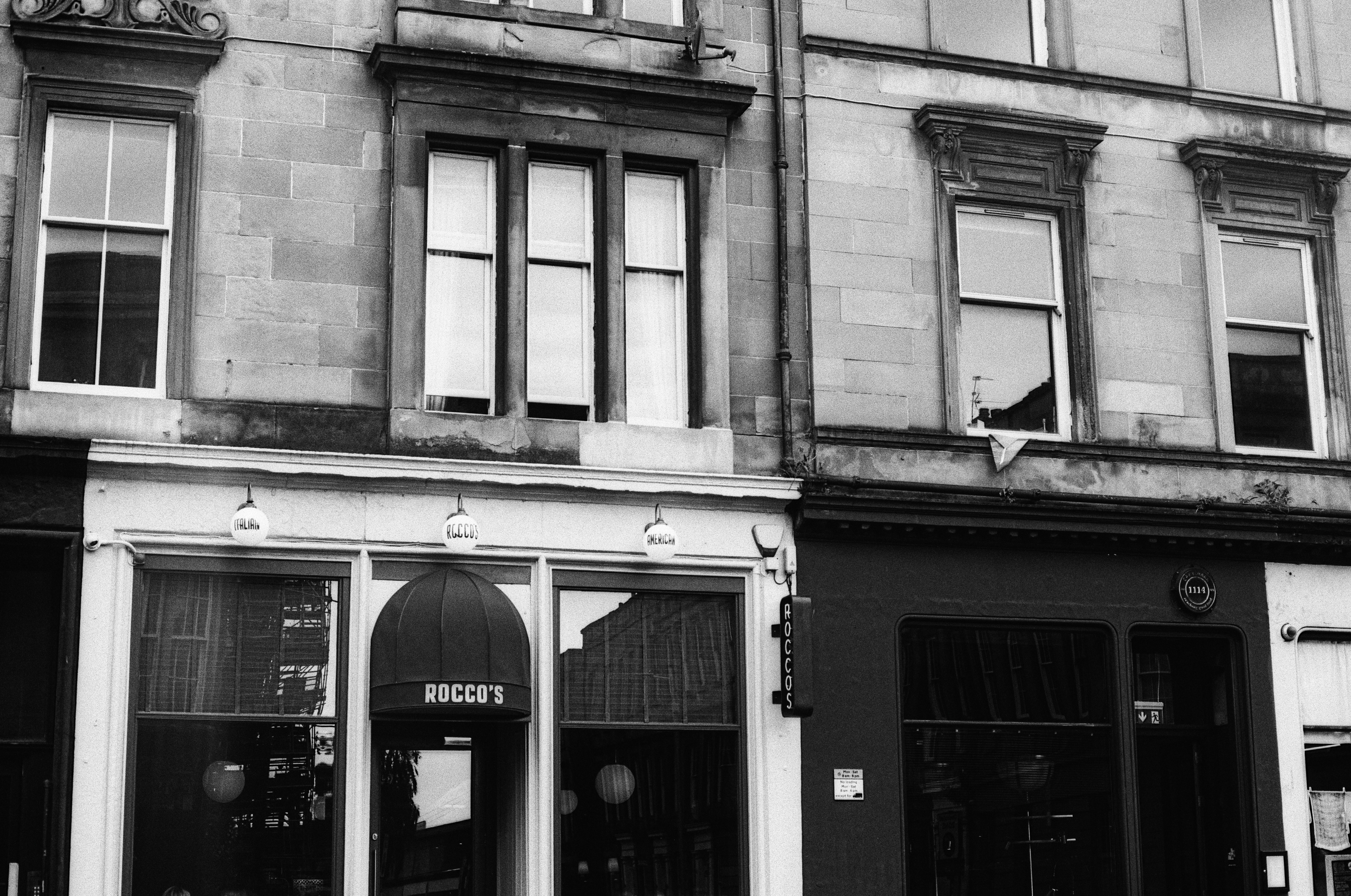 A black and white view of a storefront named Rocco's with upper floor windows