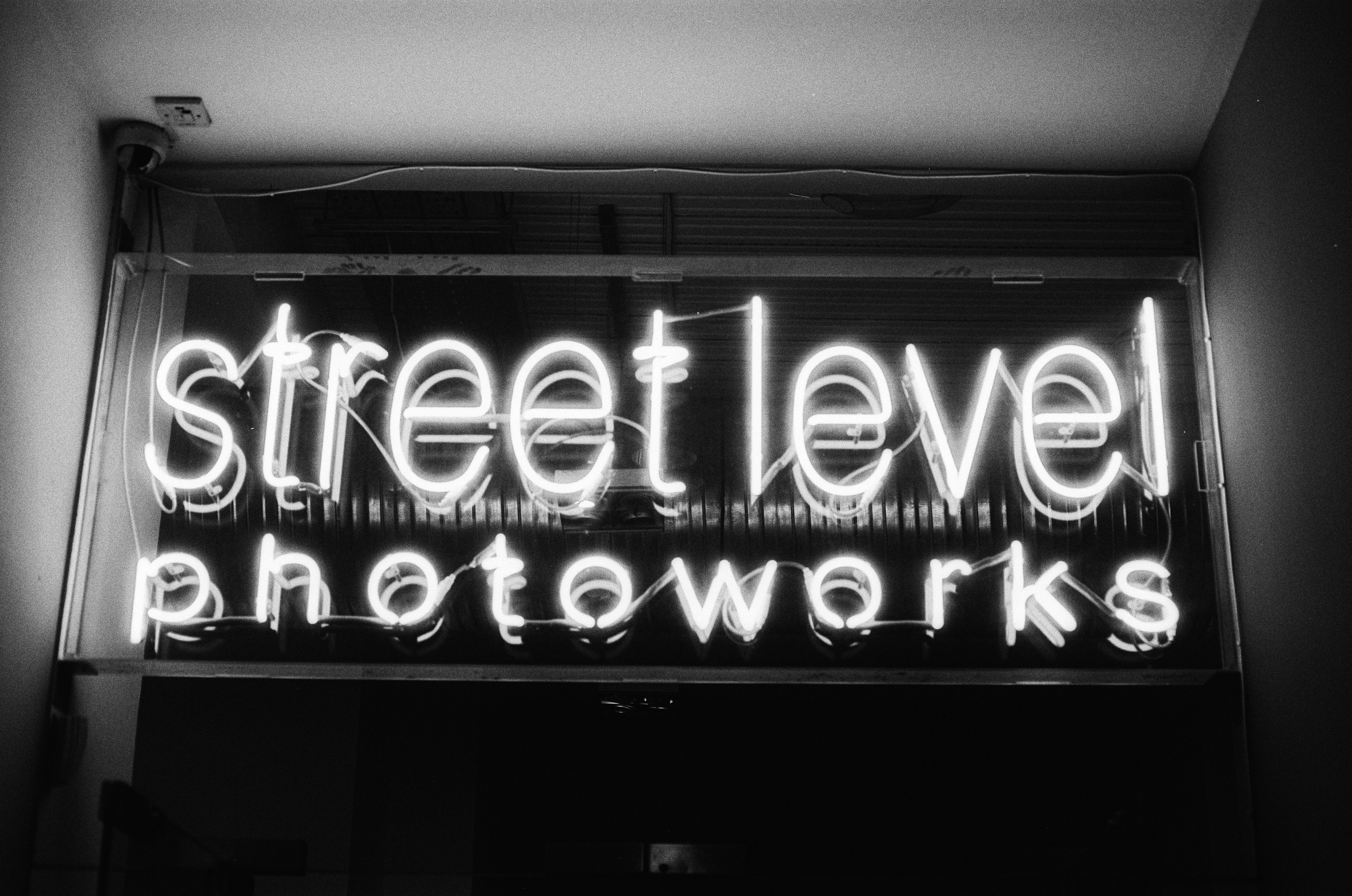 A glowing neon sign reading "street level photoworks" in a dark interior