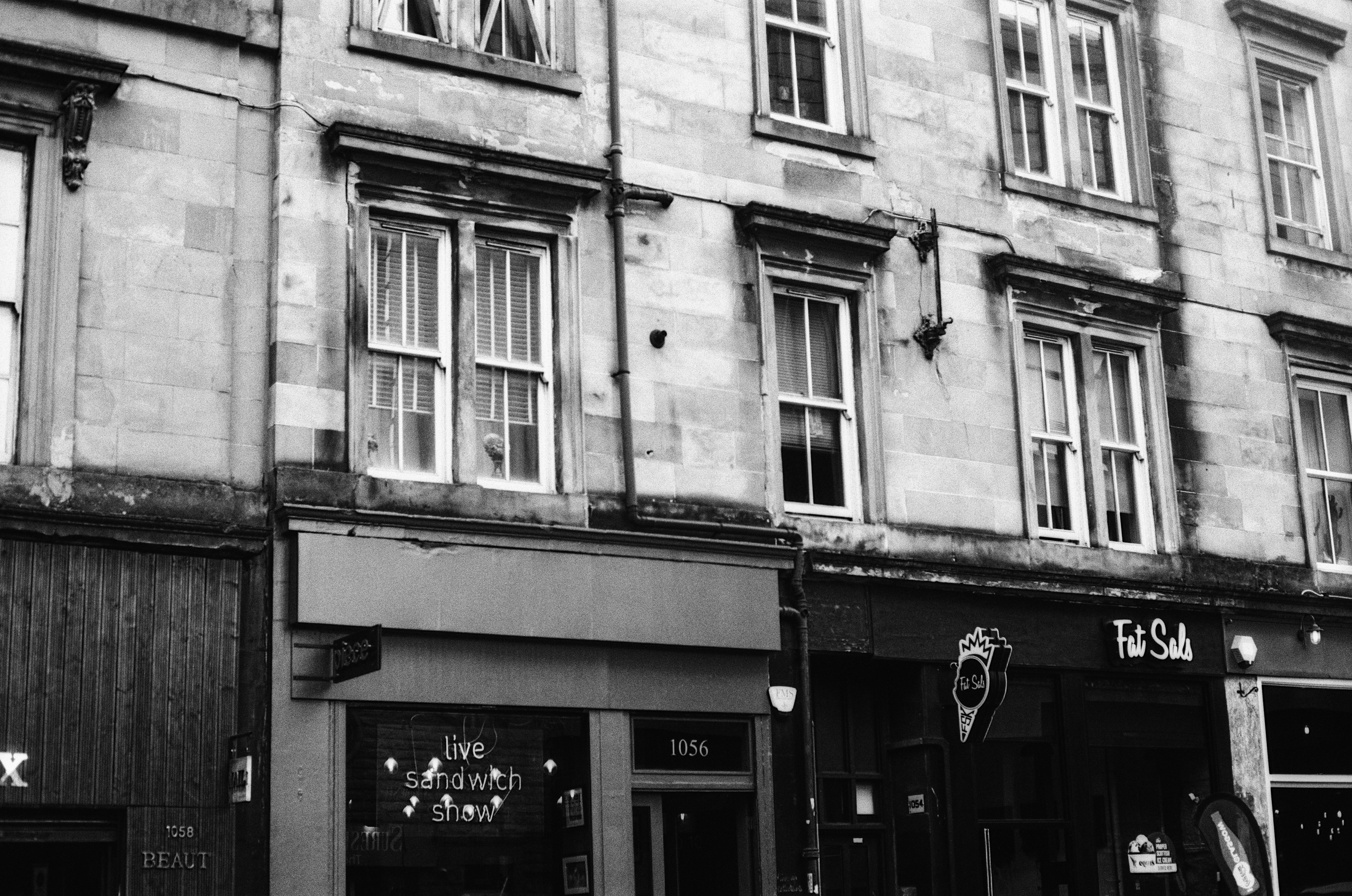 A black and white street view of stone buildings with shopfronts and windows