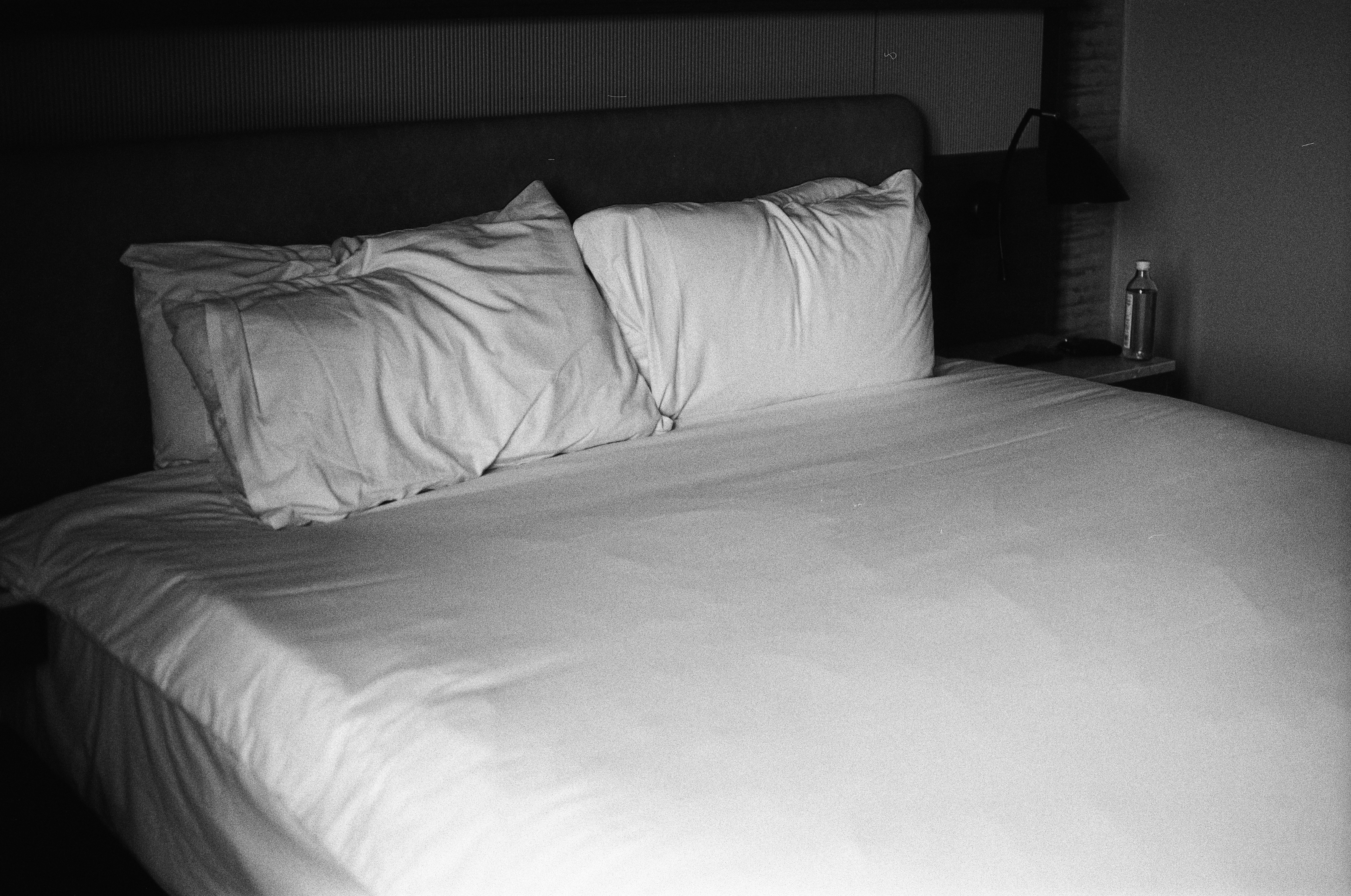 A made bed with white pillows and sheets in a dimly lit room