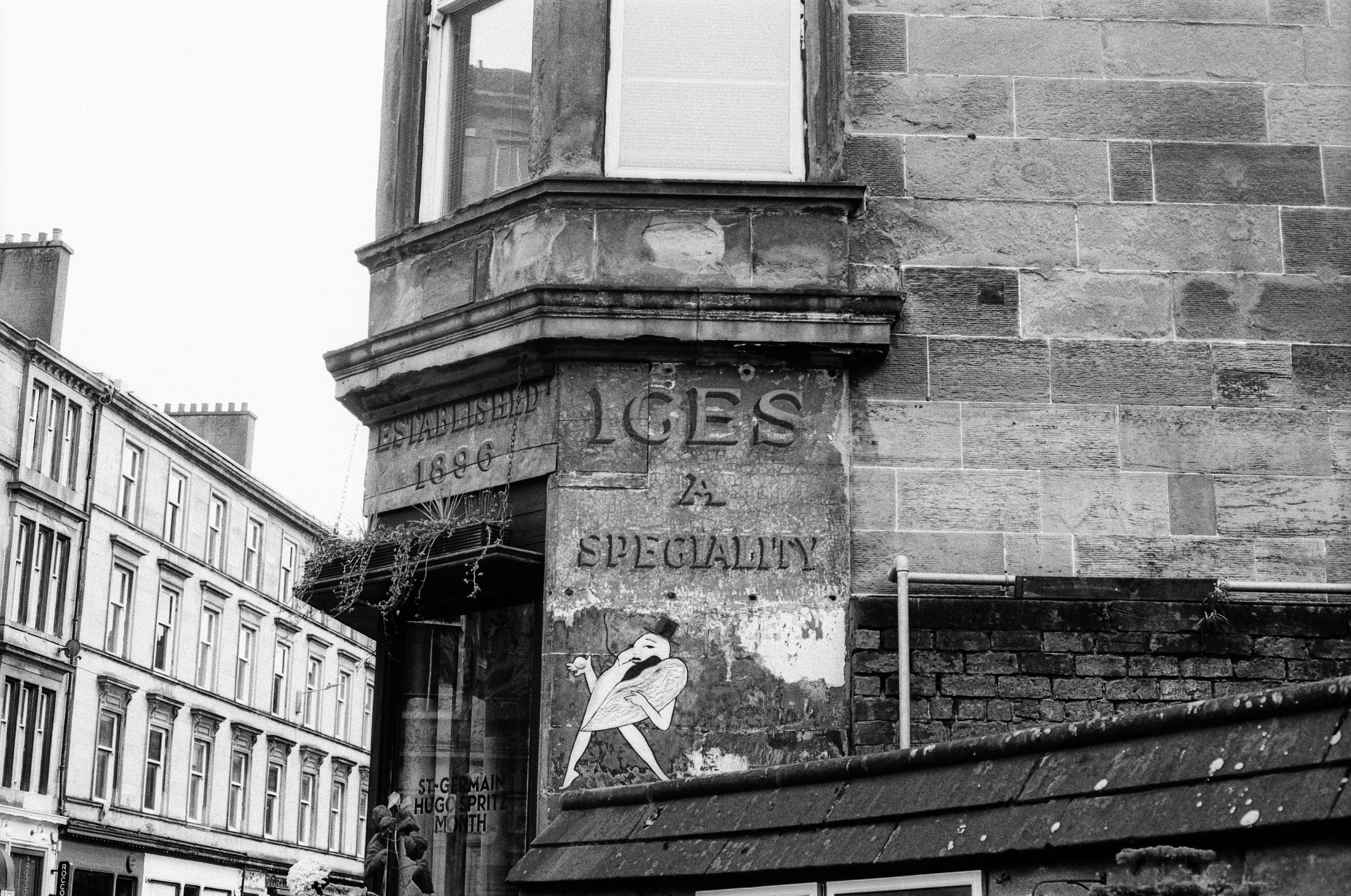 A stone building corner with faded signage reading ICES and SPECIALITY above a mural
