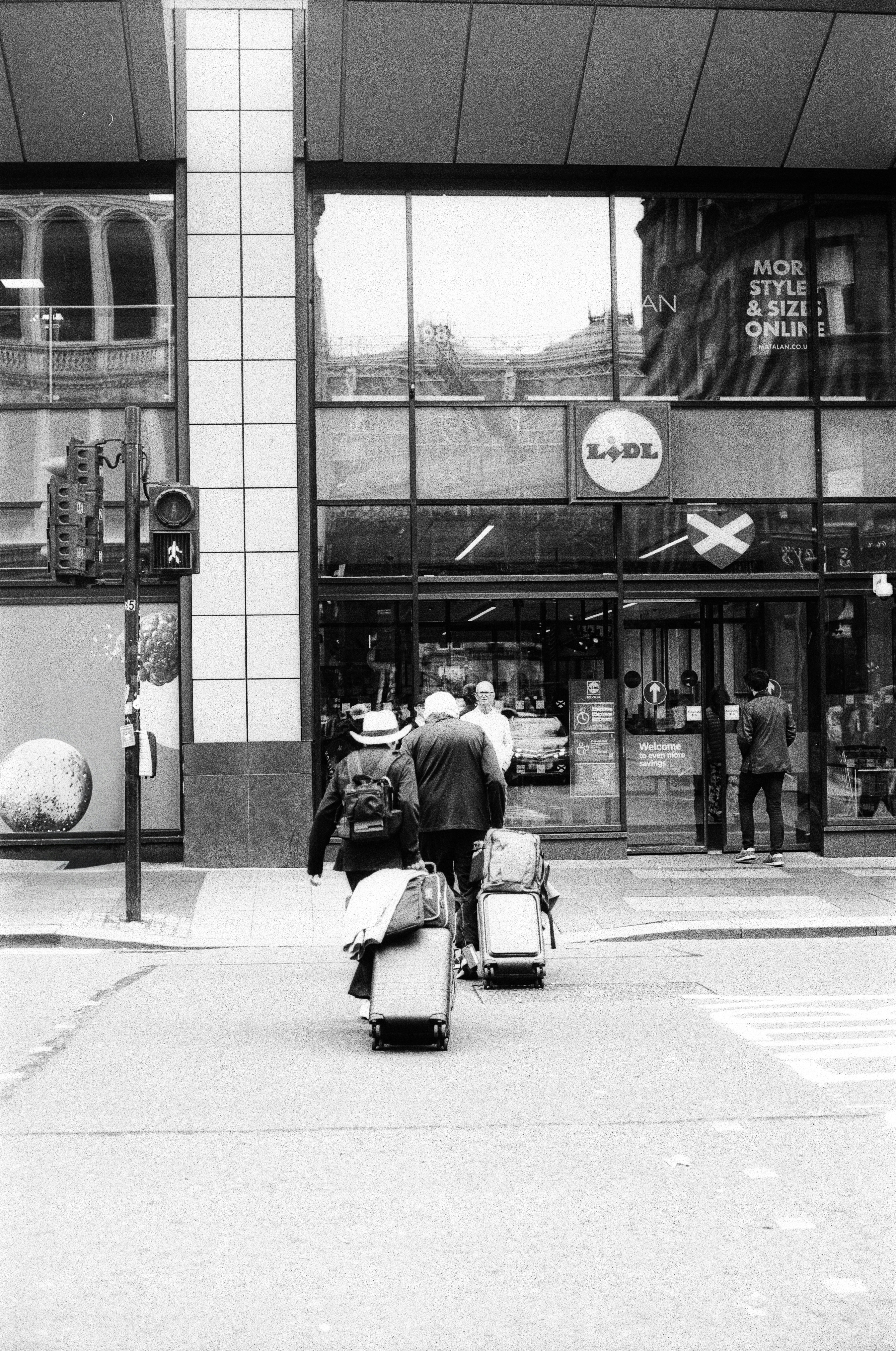 Two people with suitcases walking across a street toward a Lidl store entrance