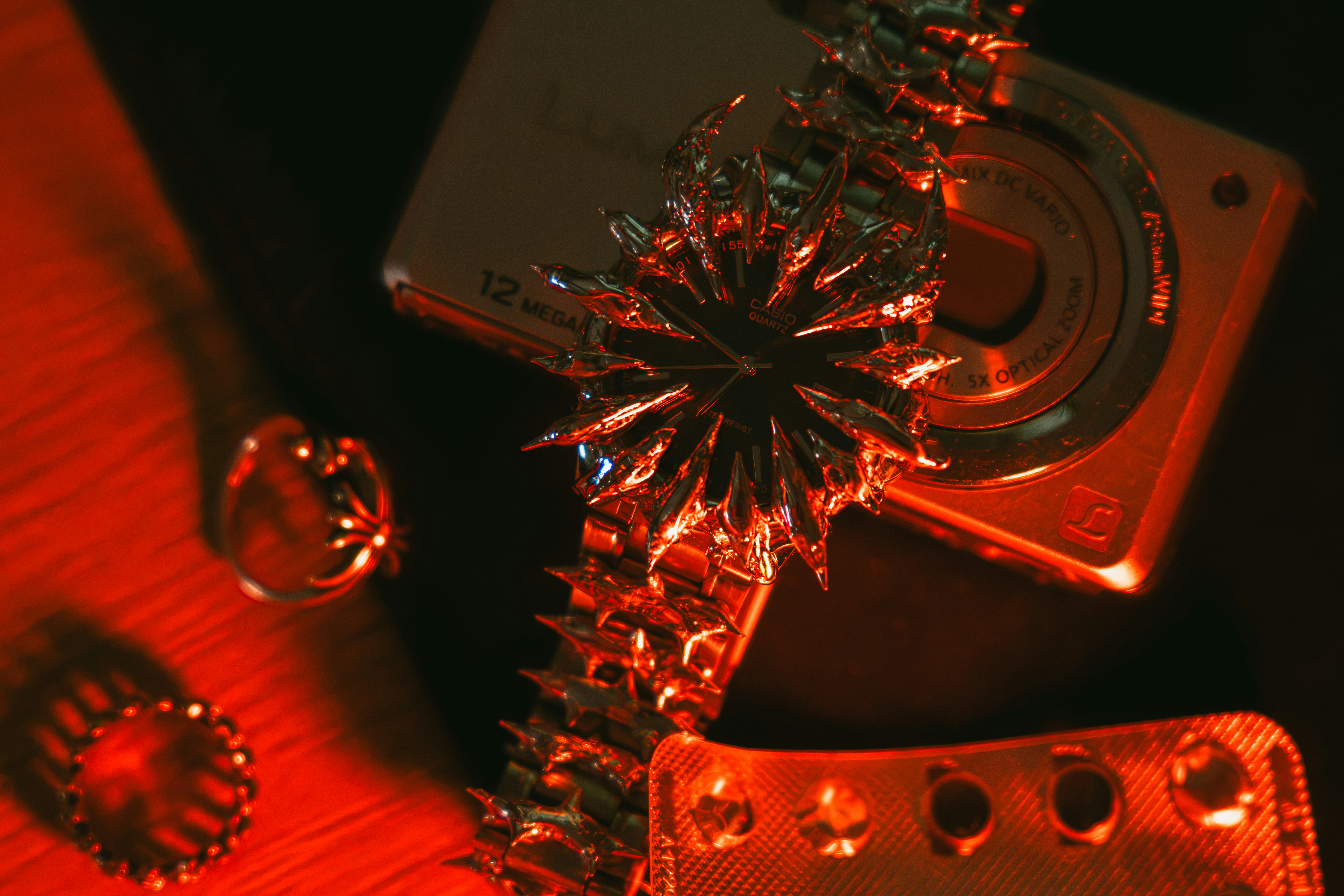 A spiked watch, rings, and a blister pack on a surface under red light