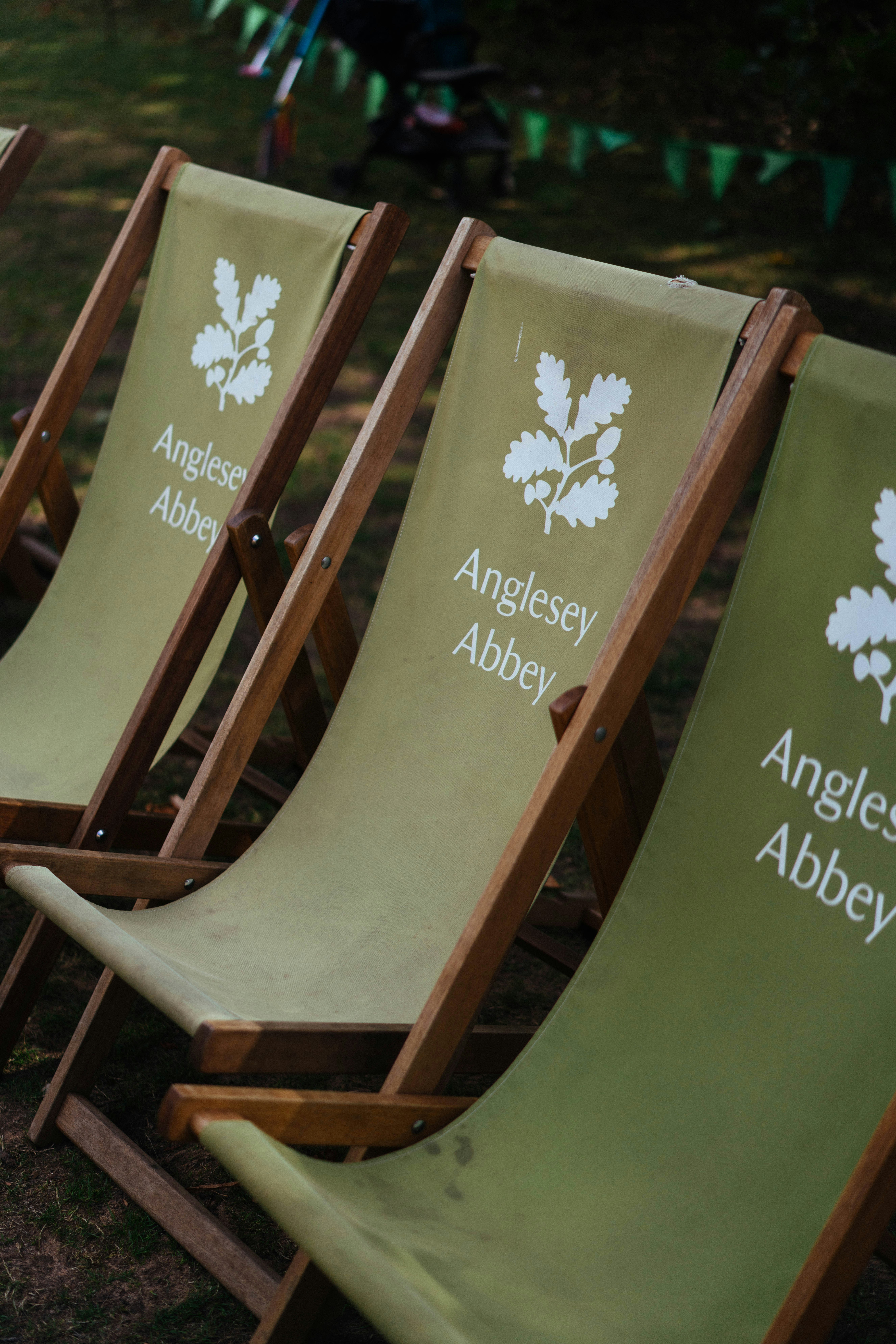 Three green wooden deck chairs with Anglesey Abbey branding on a grassy lawn
