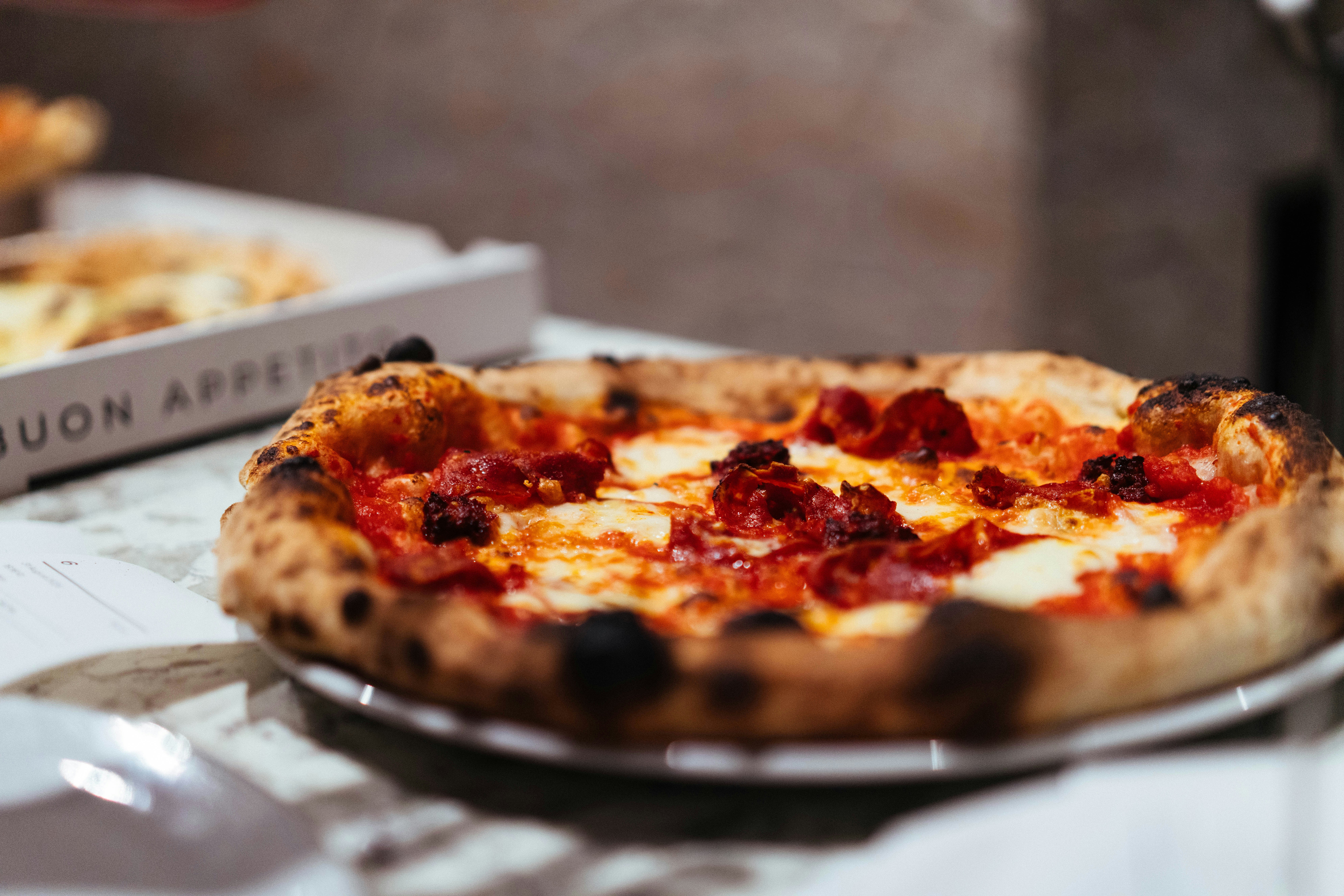 A wood-fired pepperoni pizza with melted cheese on a marble table