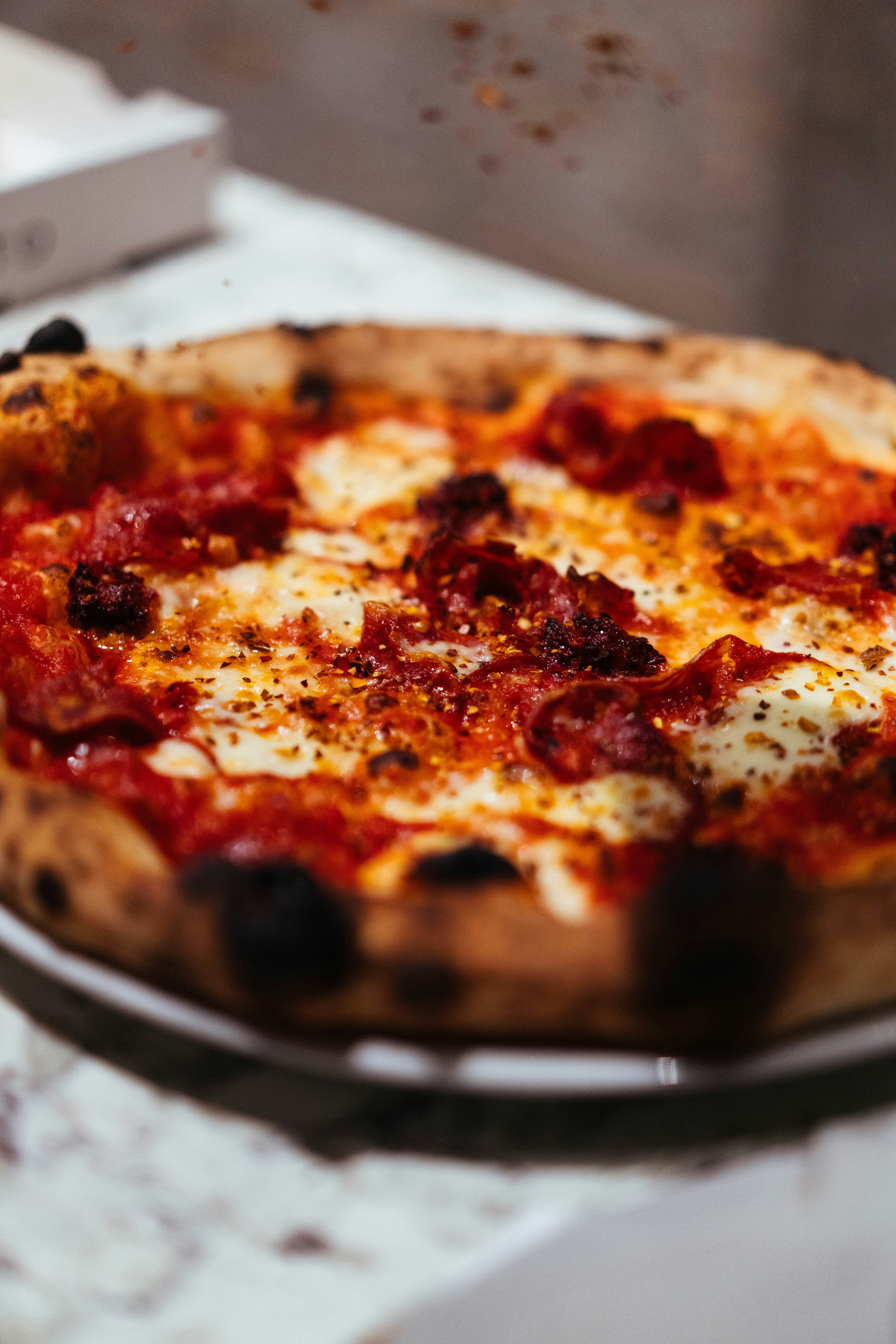 A wood-fired pizza with melted mozzarella, tomato sauce, and spicy salami on a table