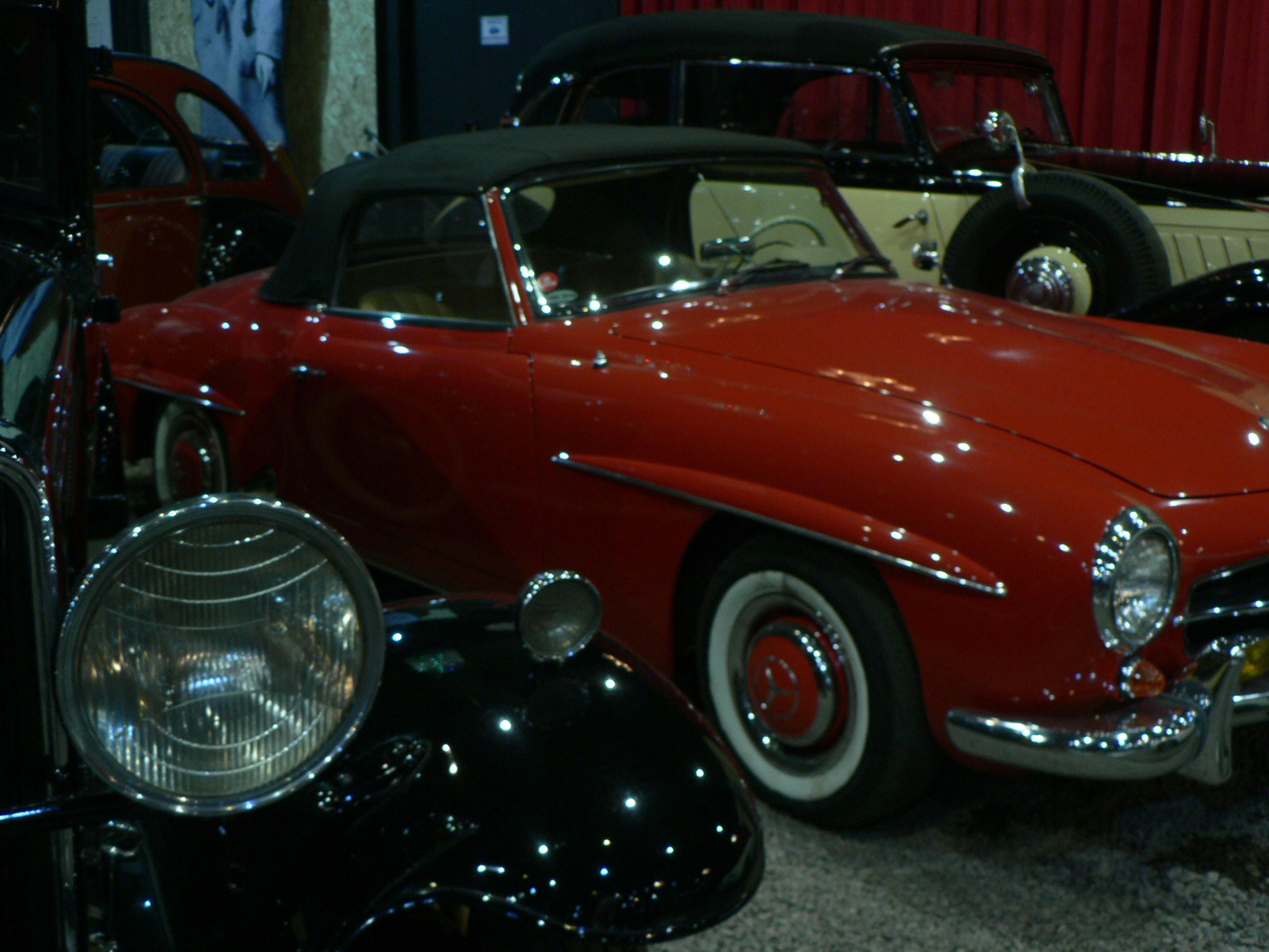 A red vintage convertible car with a black soft top in a showroom