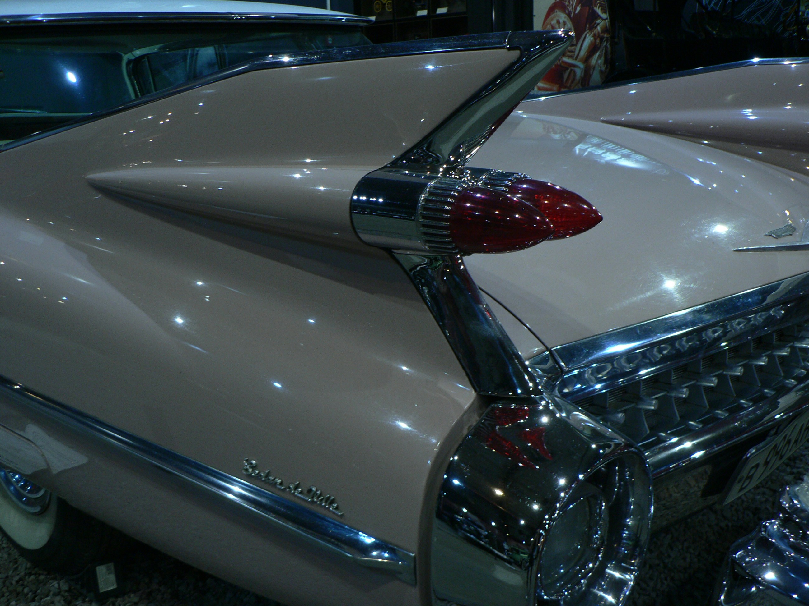 The rear tail fin and red taillights of a vintage pink Cadillac car