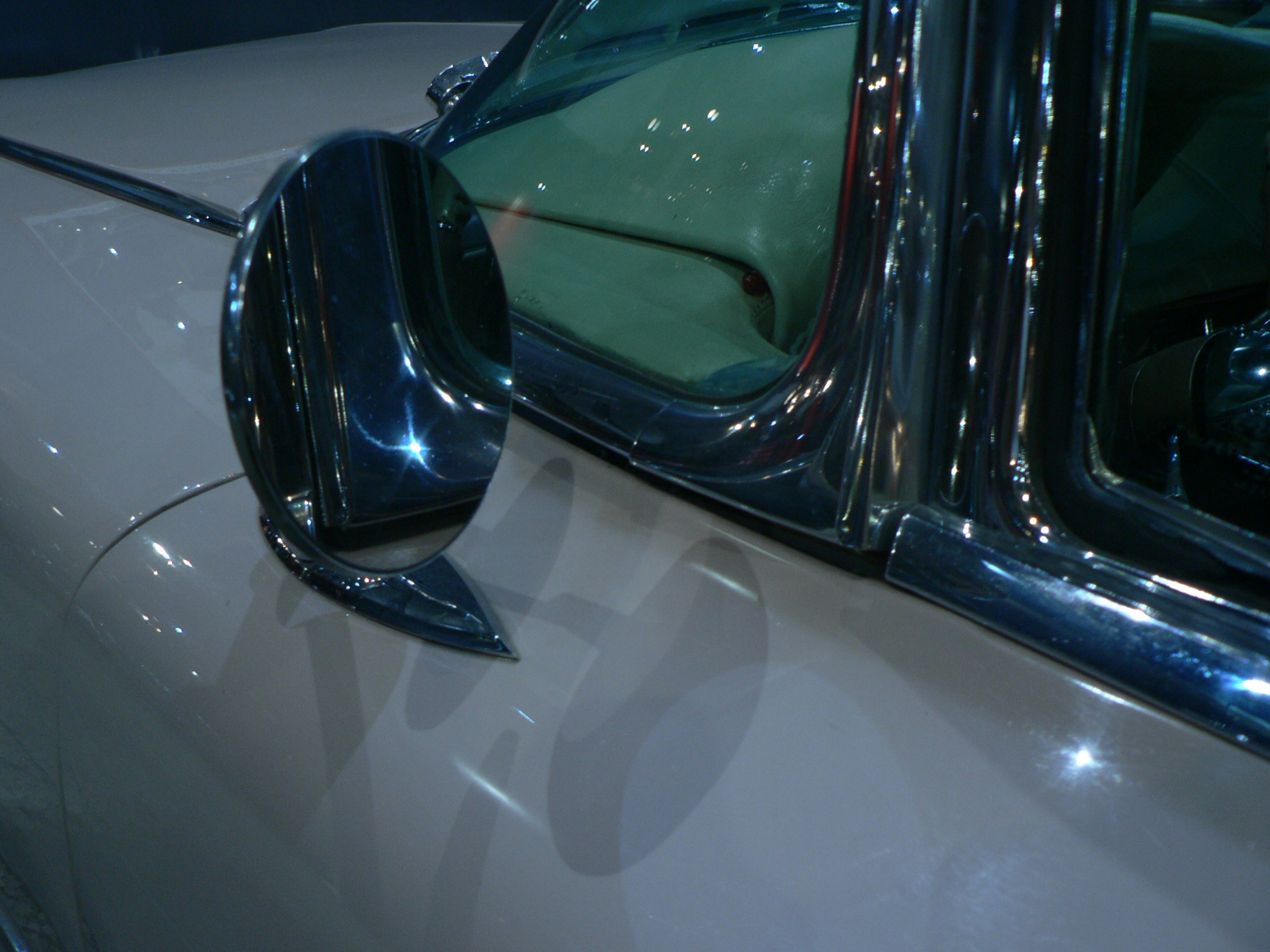 A round chrome side mirror on a vintage beige car with polished trim