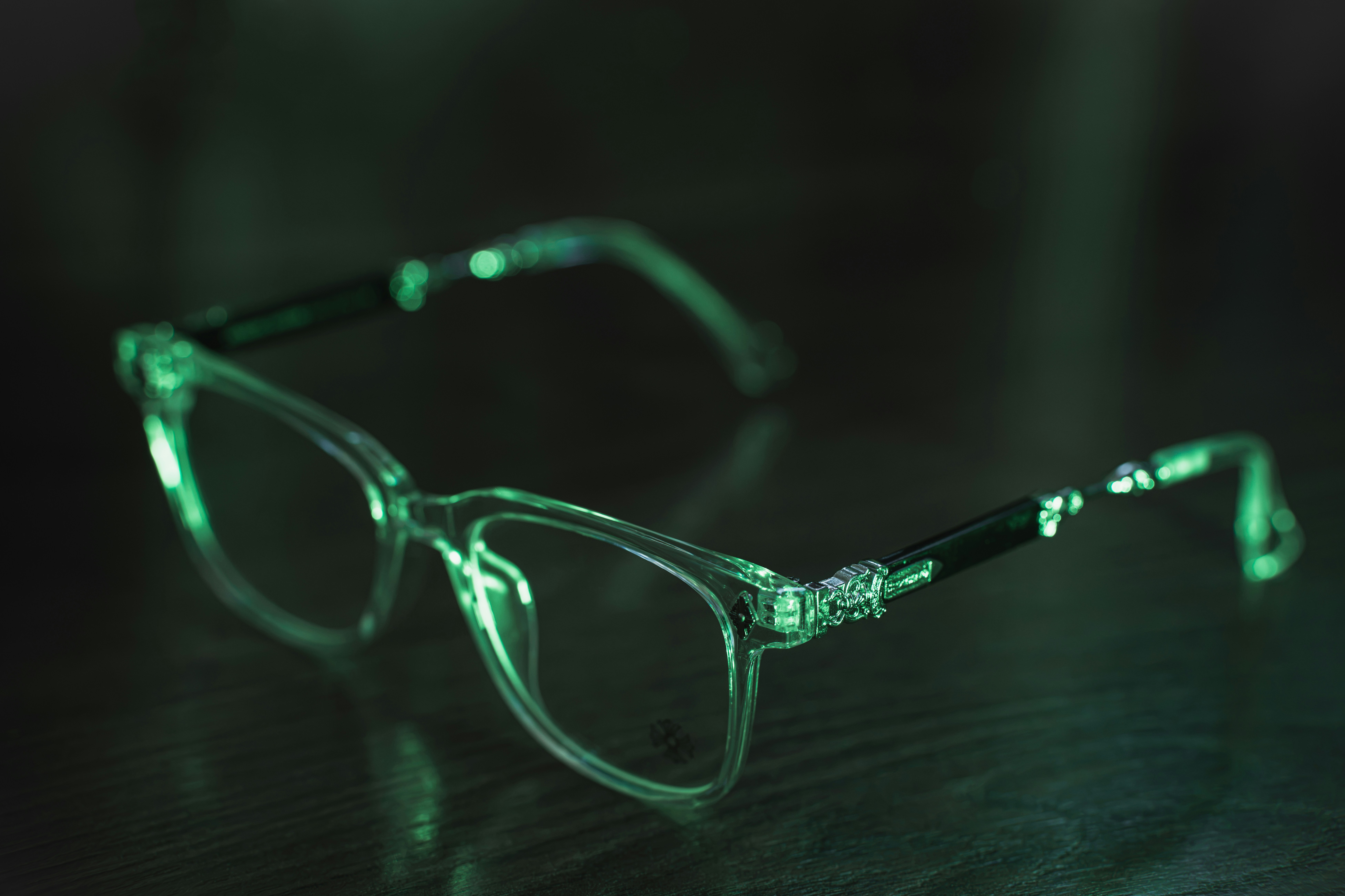 Clear eyeglasses with dark temples illuminated by a vibrant green light on a table