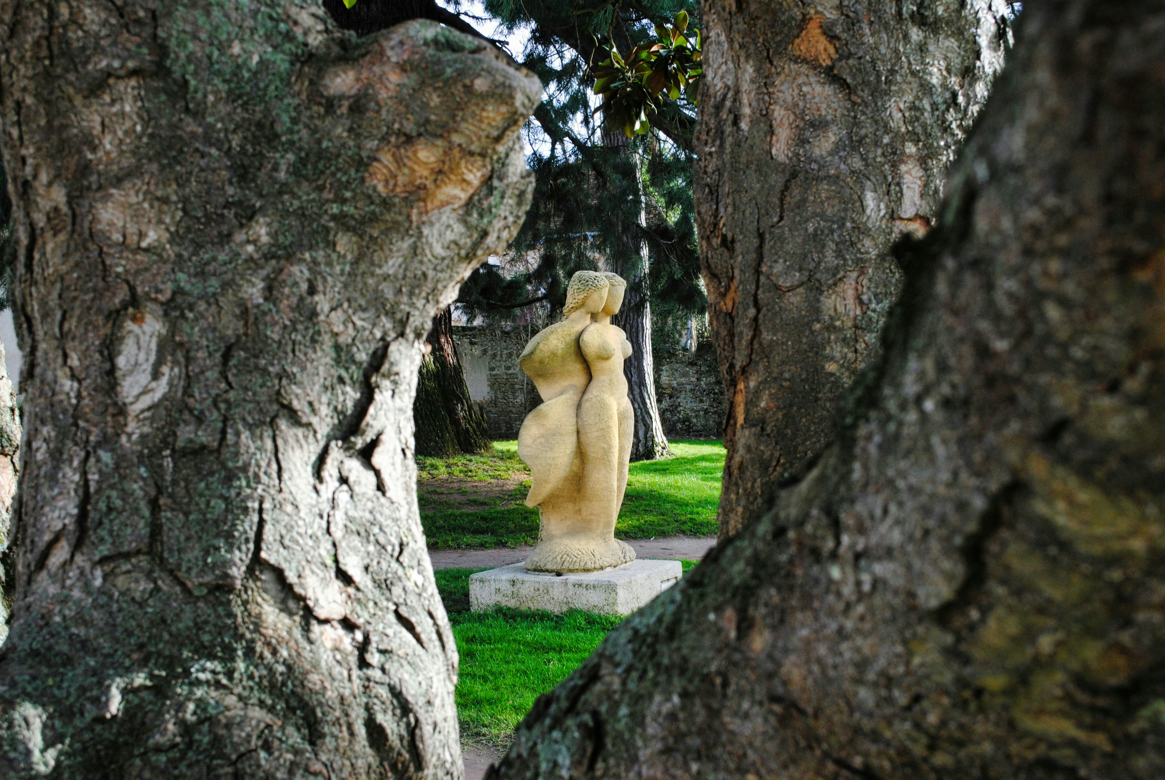 A stone sculpture of two figures standing together in a park between trees