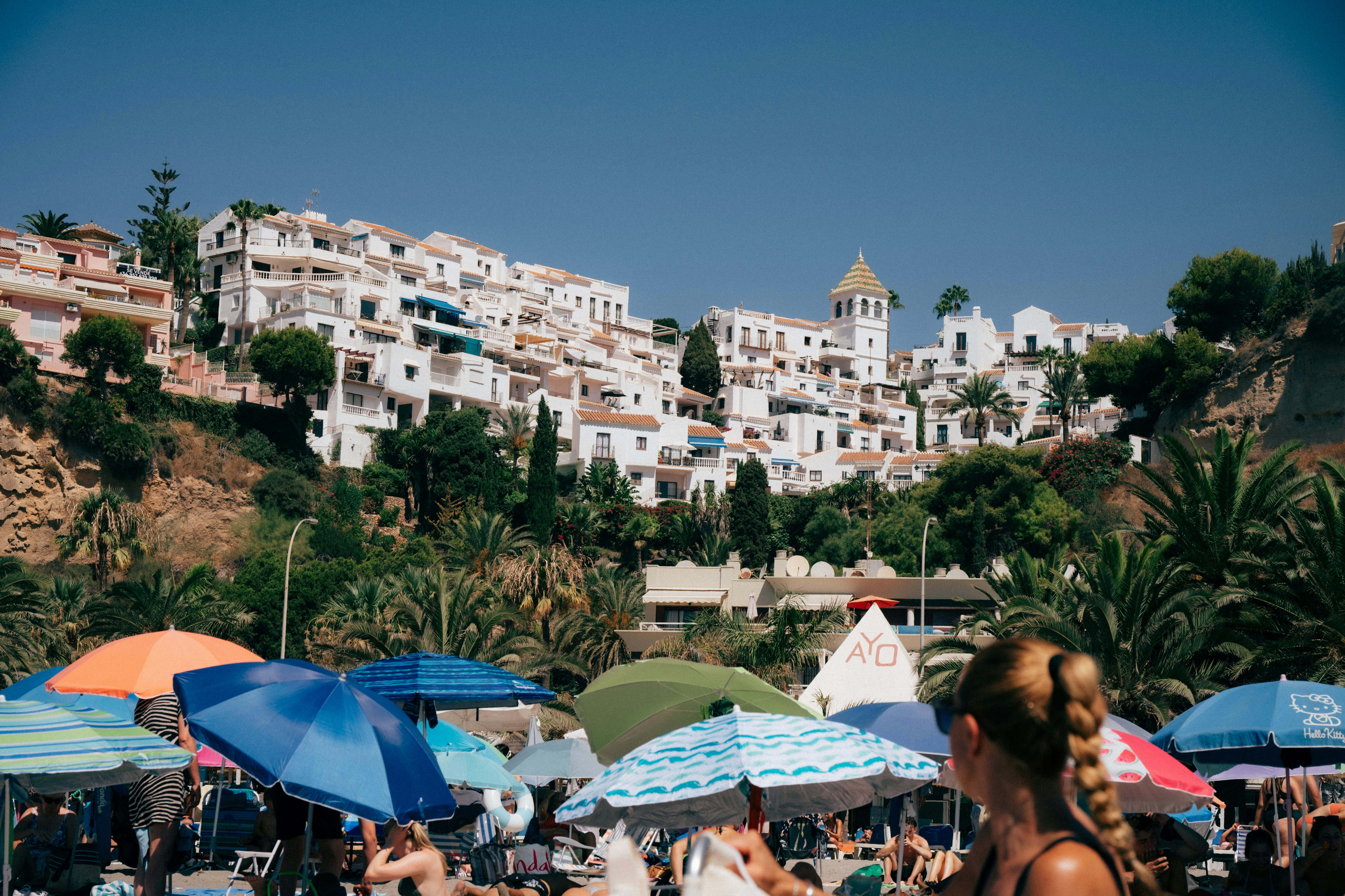Colorful beach umbrellas on a sandy shore below white hillside houses