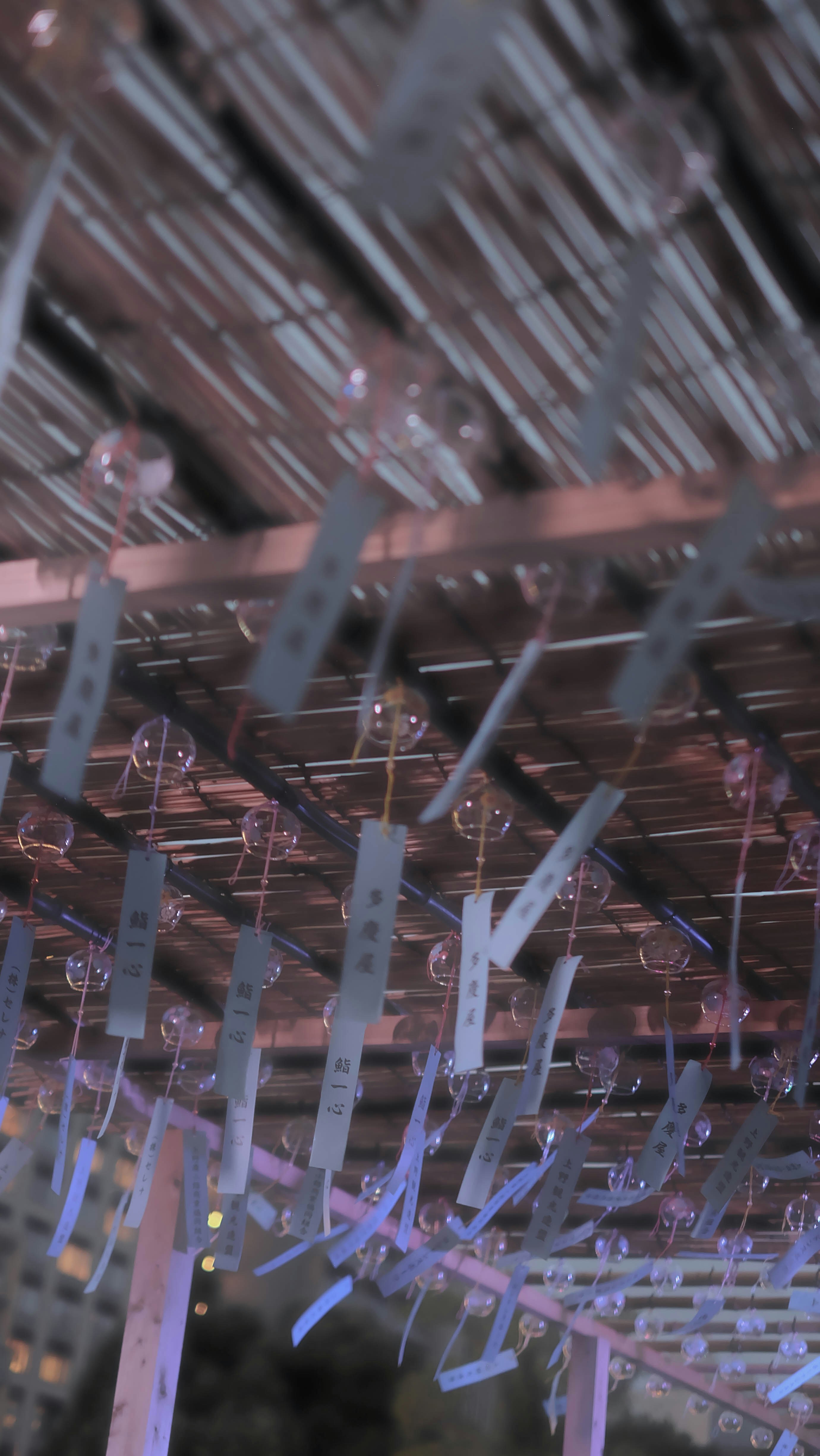 Glass wind chimes with paper strips hanging from a bamboo ceiling