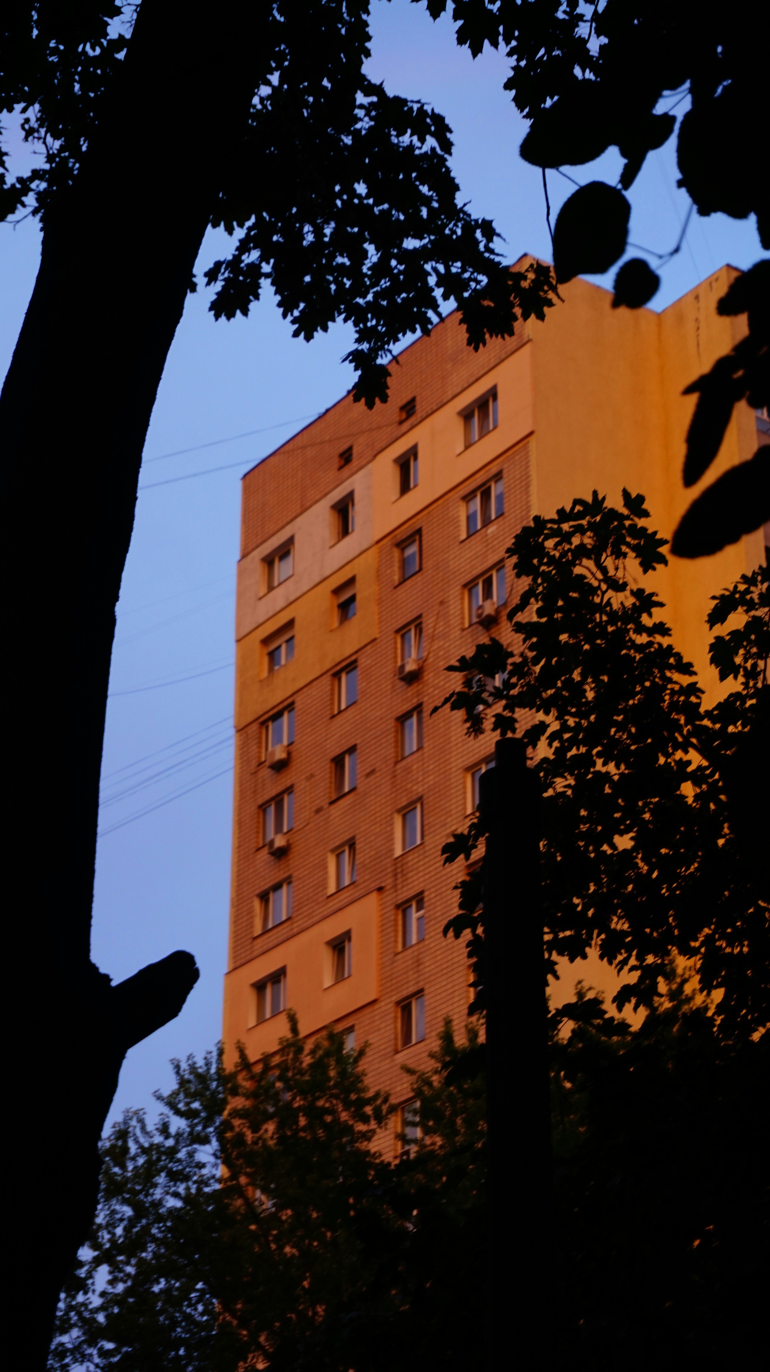 Ein hohes Wohnhaus, erleuchtet von warmem Licht gegen einen blauen Abendhimmel