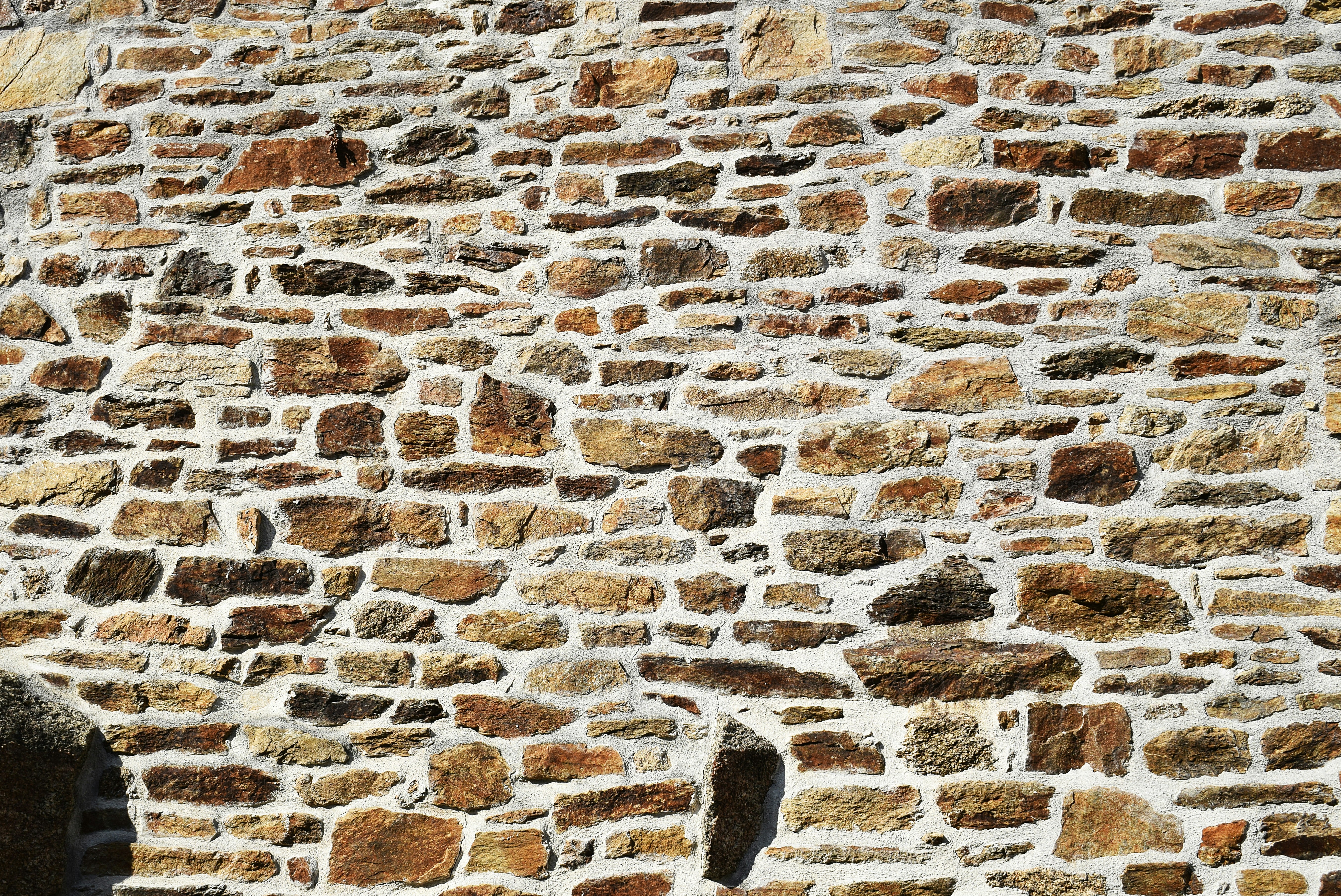 A rustic wall made of irregular brown and tan stones with white mortar
