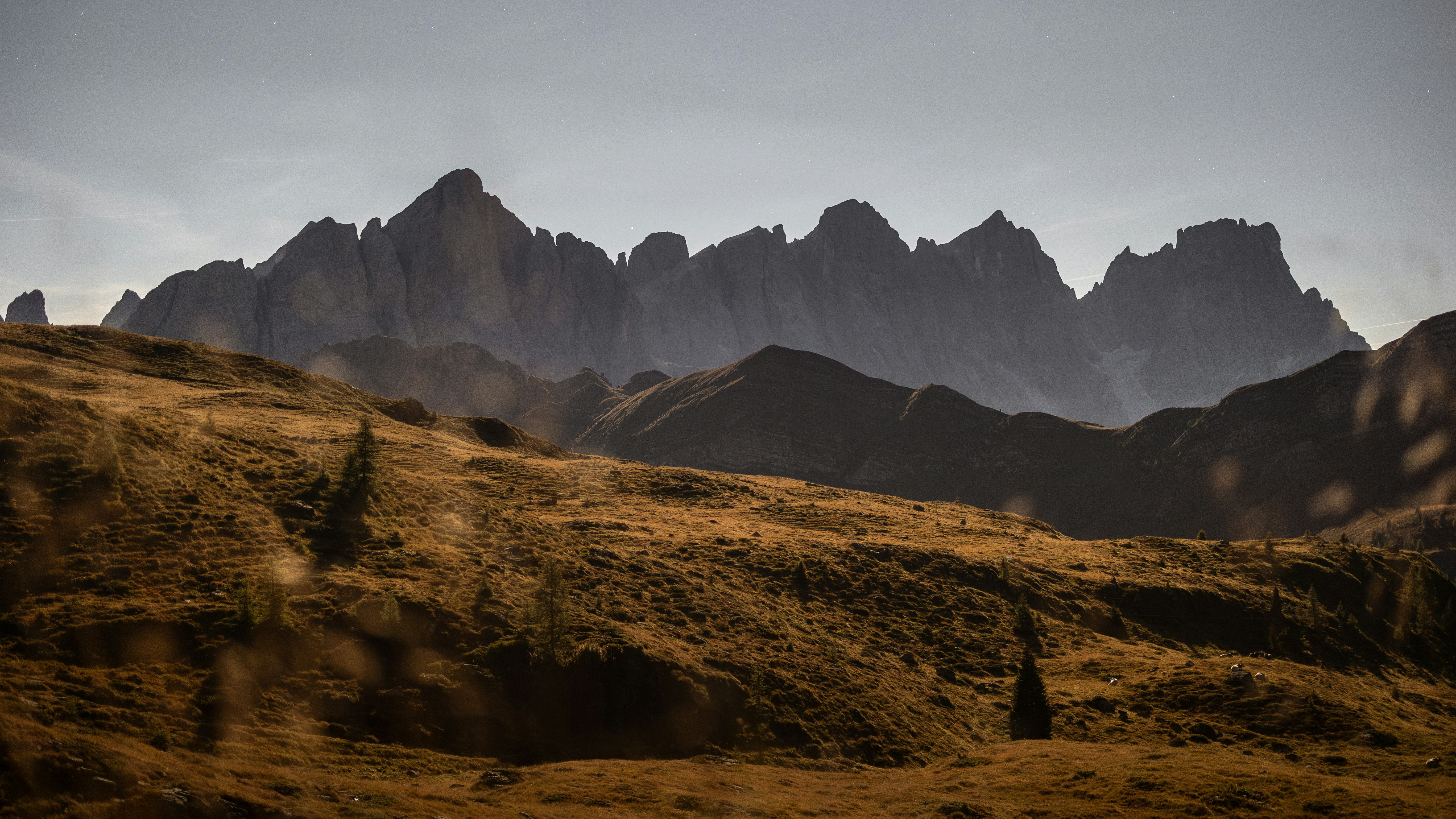 Jagged mountain peaks rising above a rolling golden brown alpine meadow
