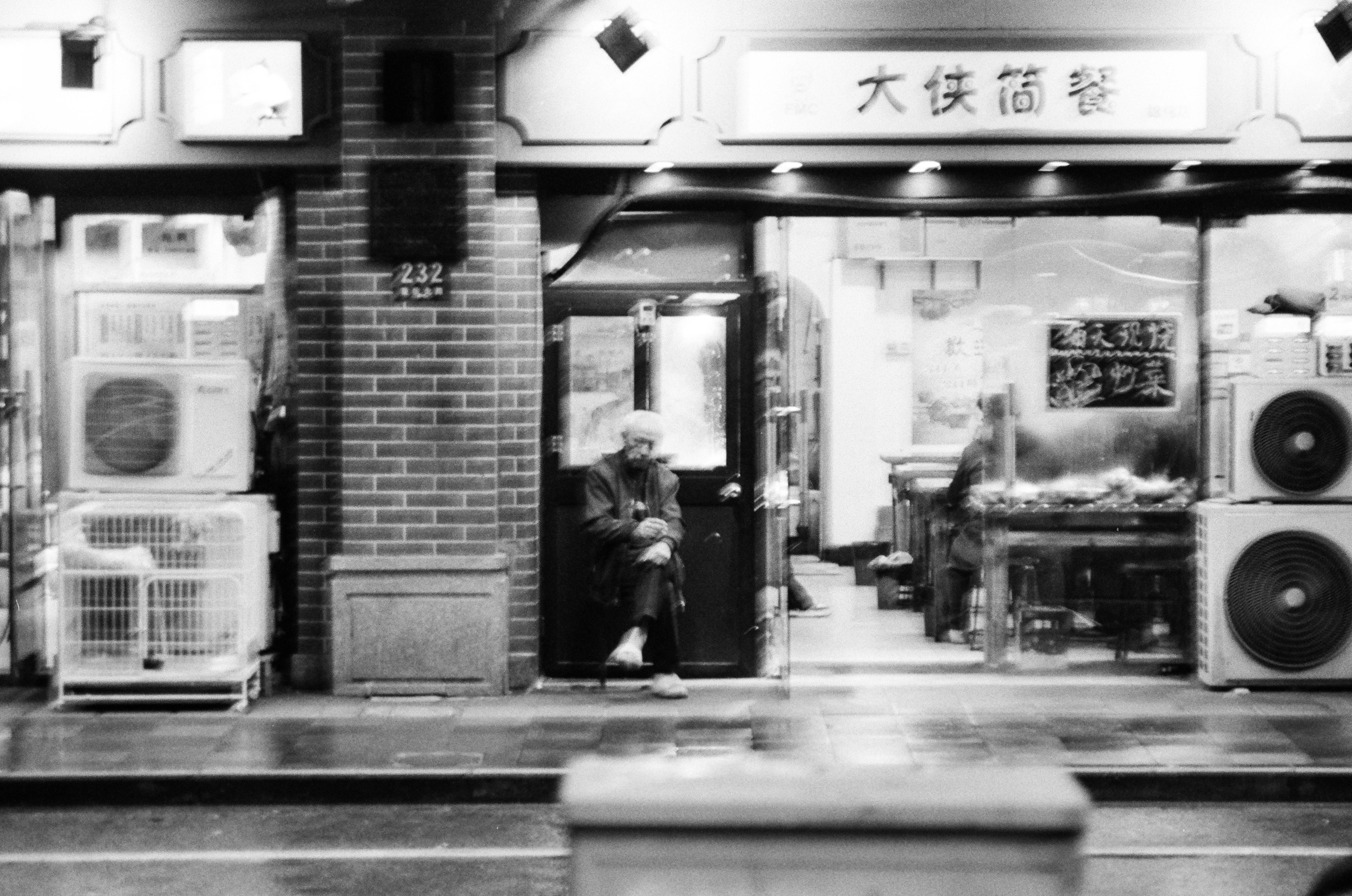 A person sitting in a doorway of a restaurant at night in black and white