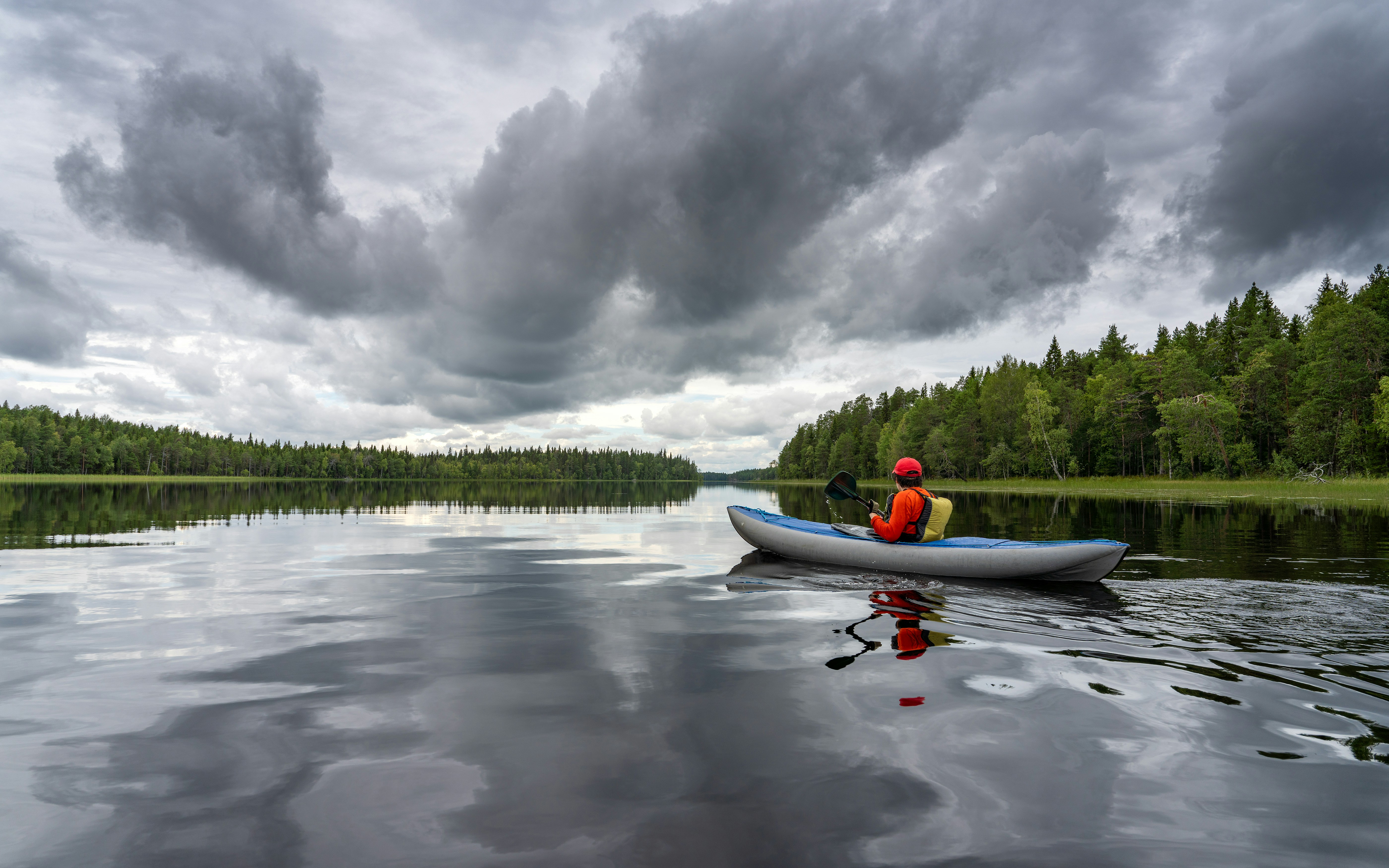 A person in a red shirt kayaking on a calm lake under cloudy skies