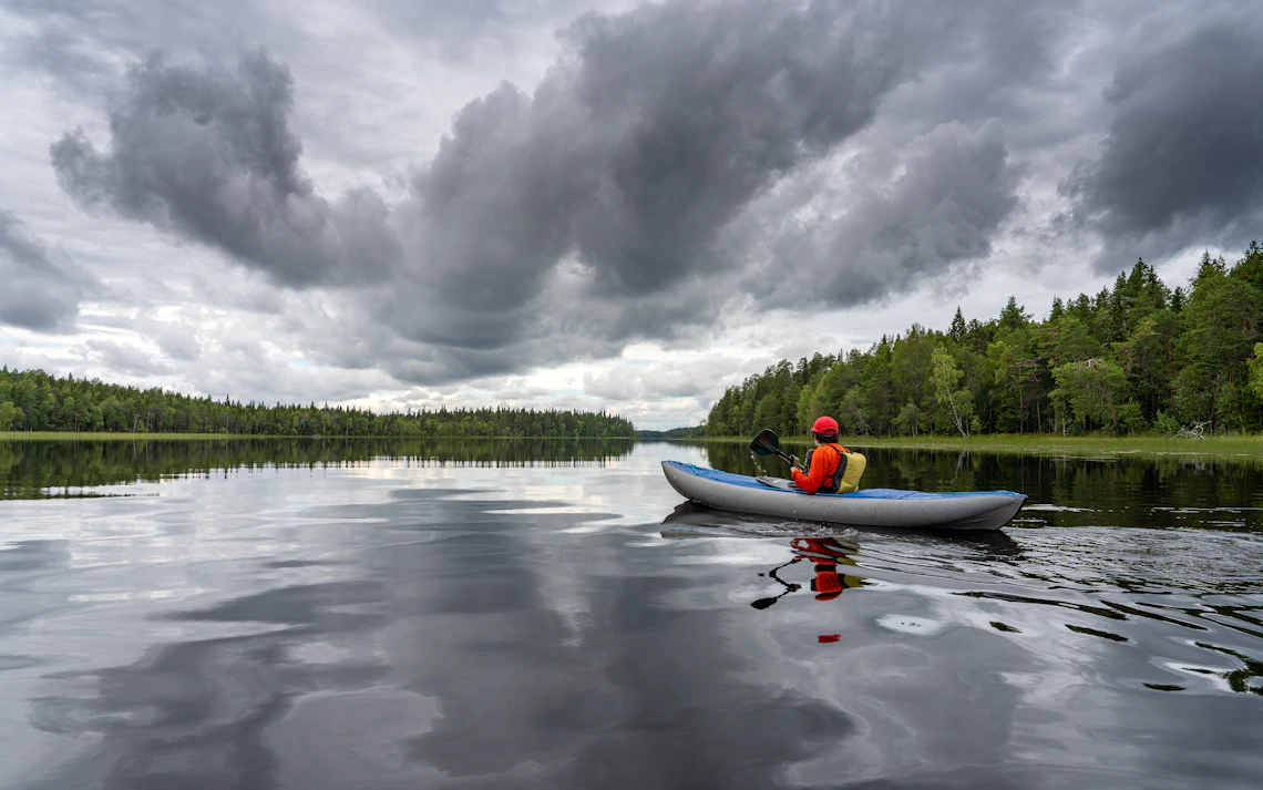 Kayaker wearing safety equipment paddling across a quiet forest lake