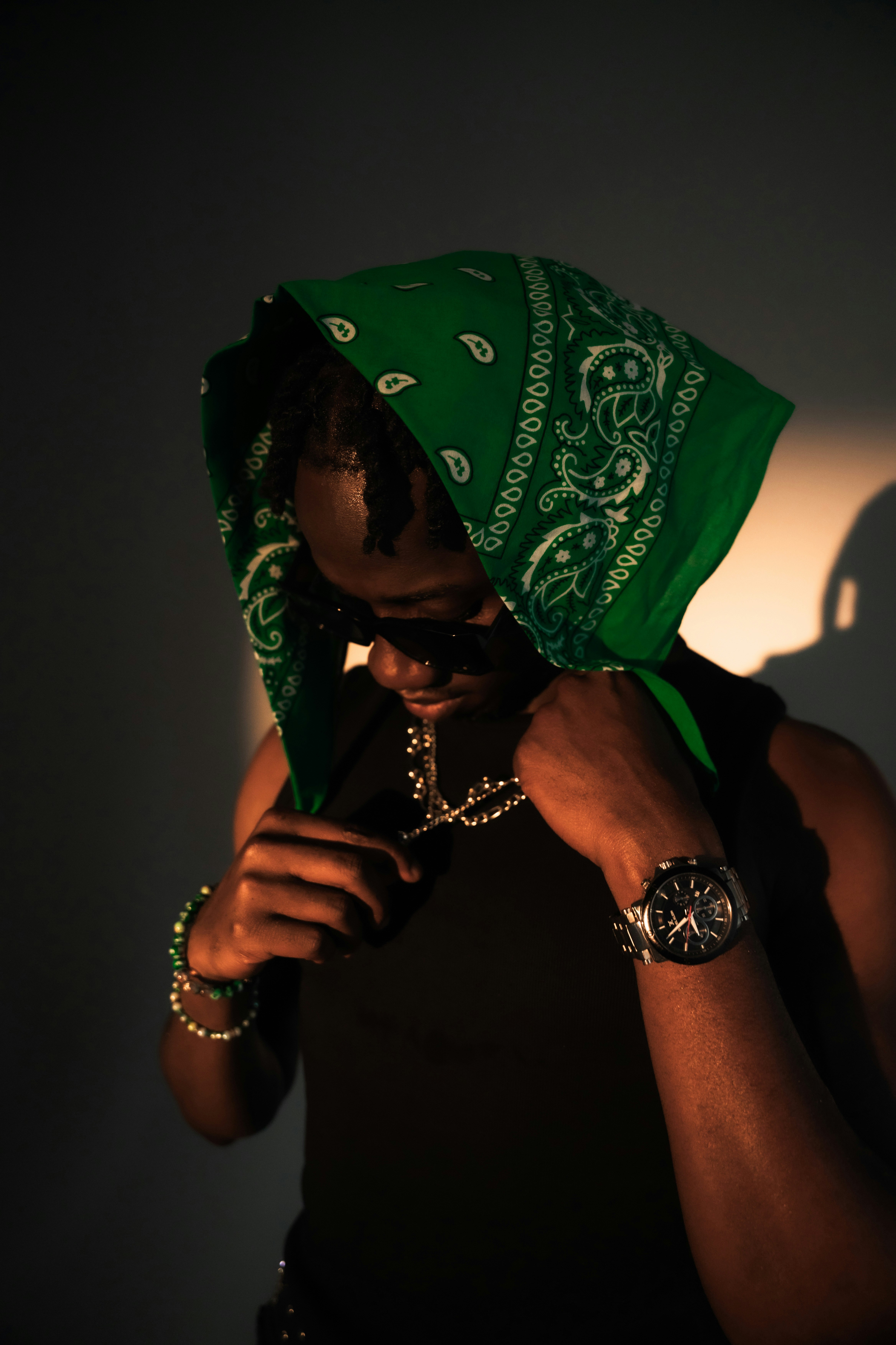 A person wearing a green paisley bandana and sunglasses in warm side lighting