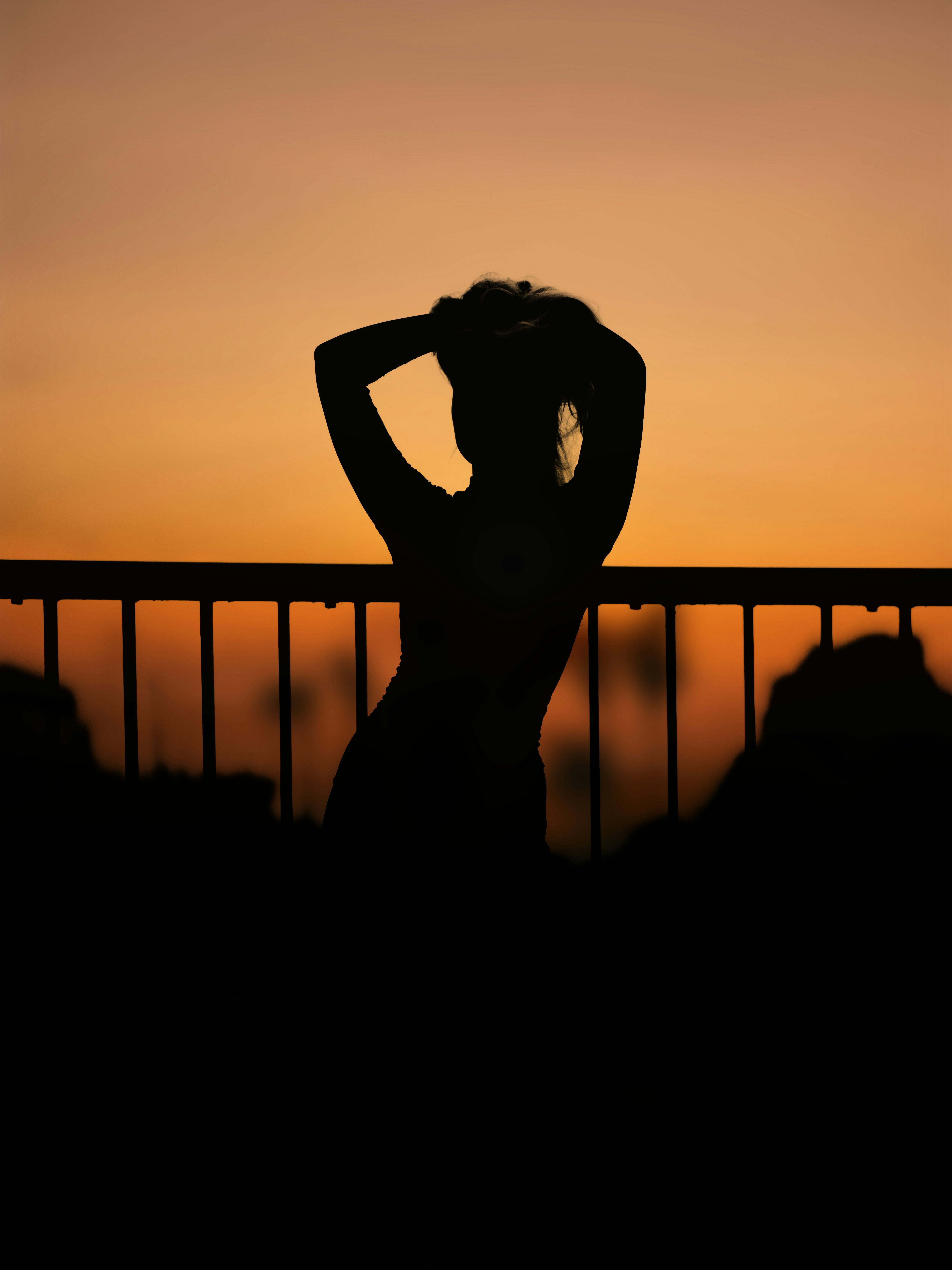 A person in silhouette against a warm orange sky, hands behind their head