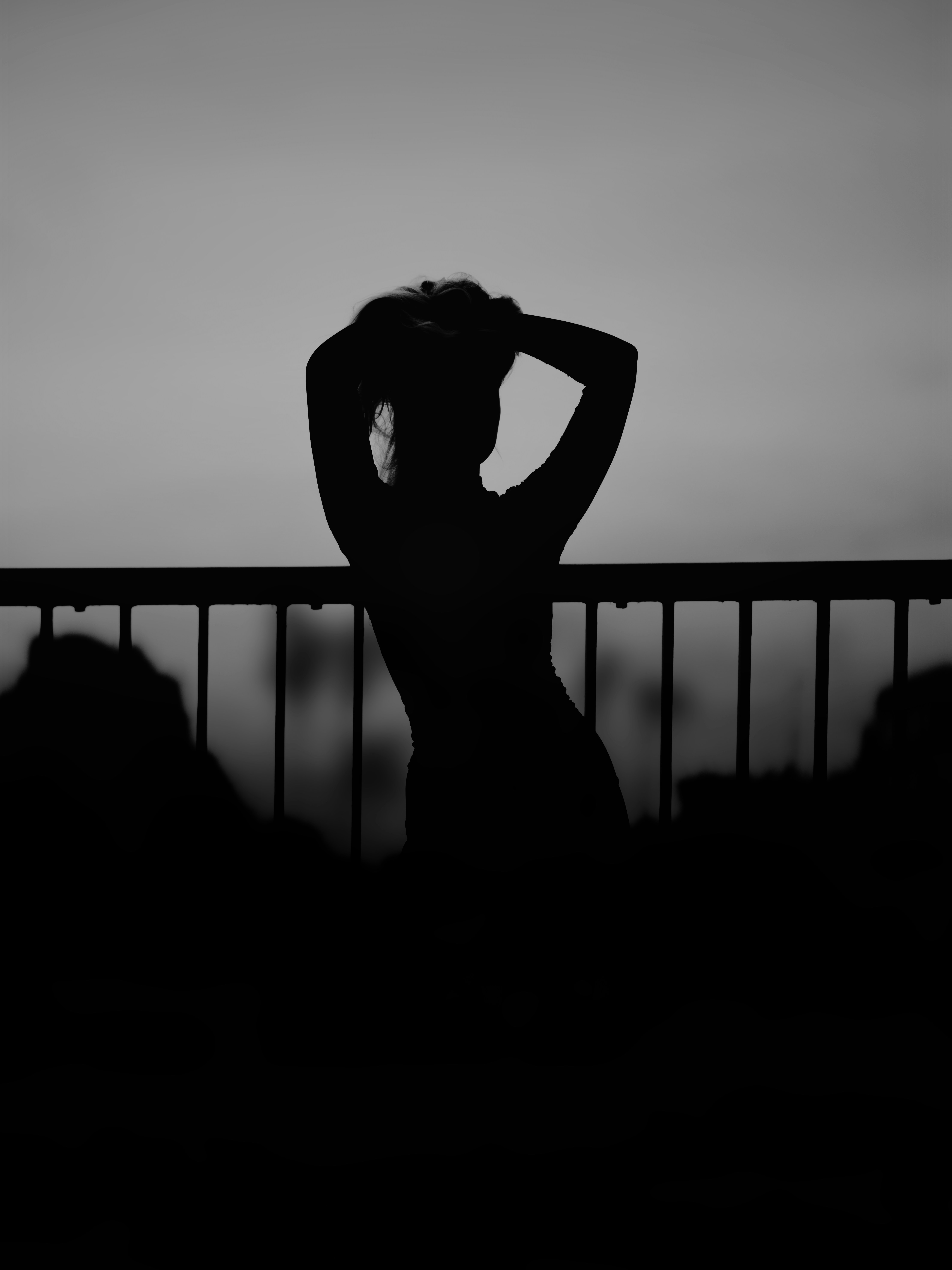 A person in silhouette with hands behind their head against a railing