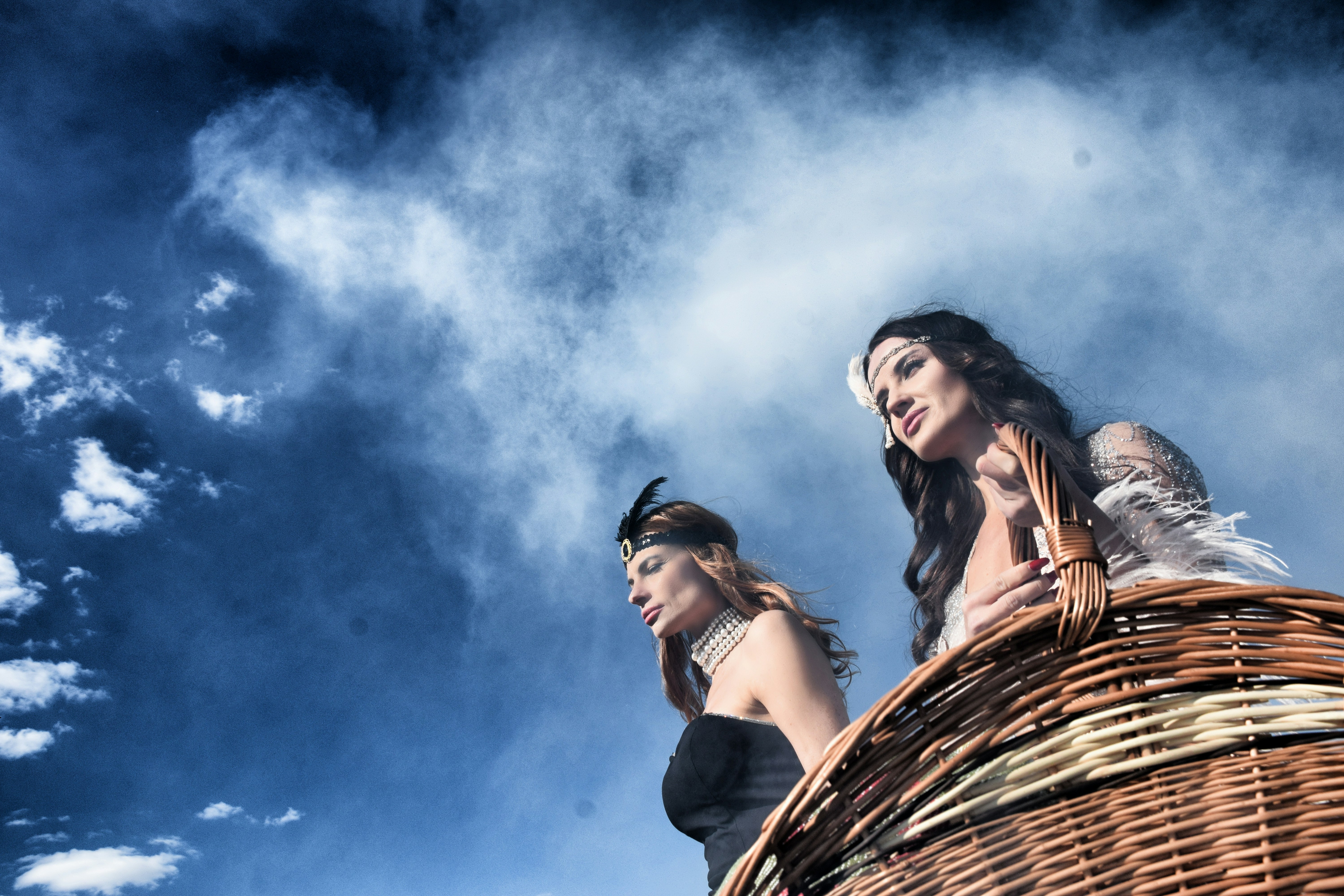 Dos mujeres con atuendo vintage de flapper sosteniendo una cesta de mimbre contra un cielo azul