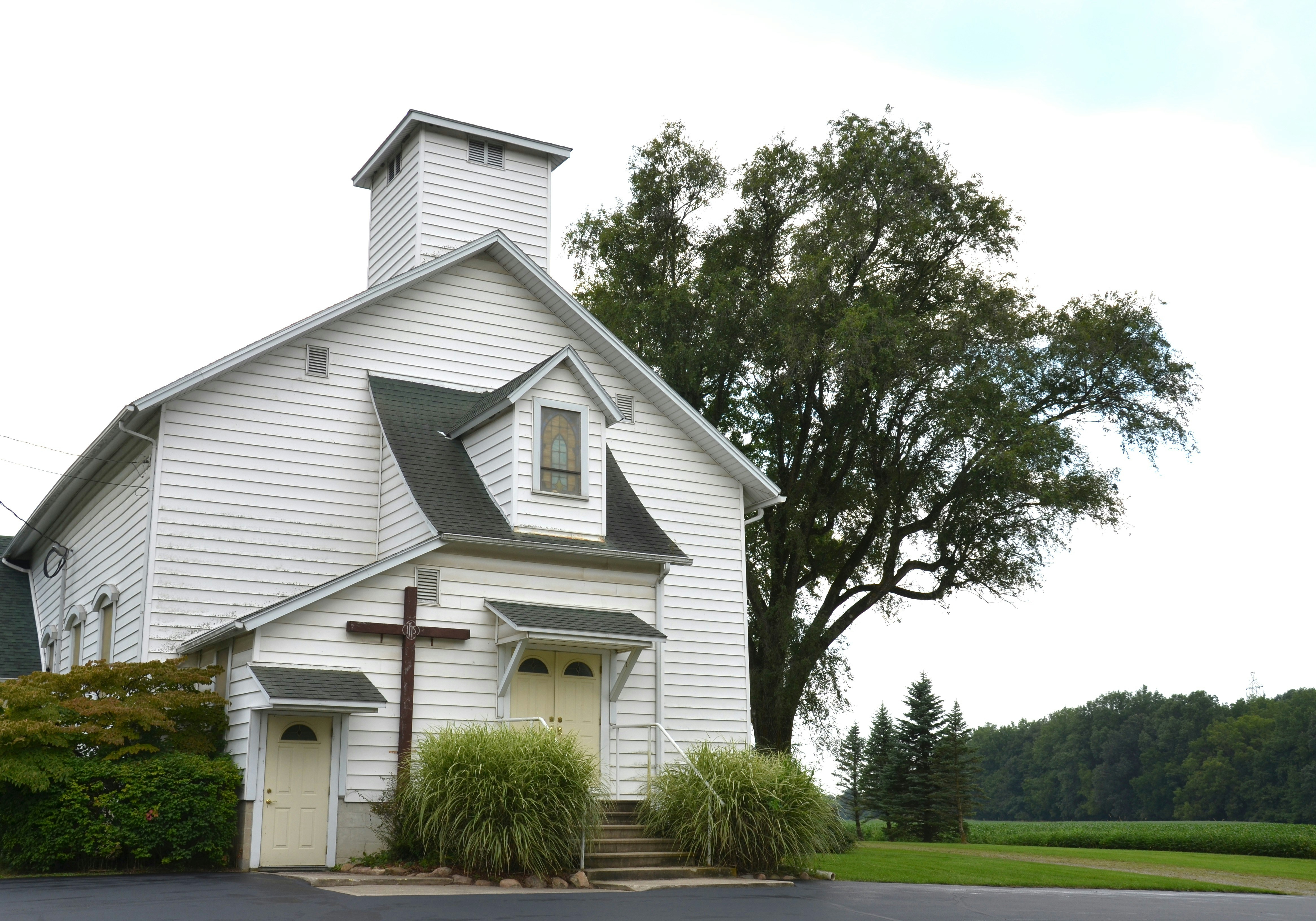 Eine weiße Holzkirche mit einem Kreuz an der Wand neben einem großen Baum