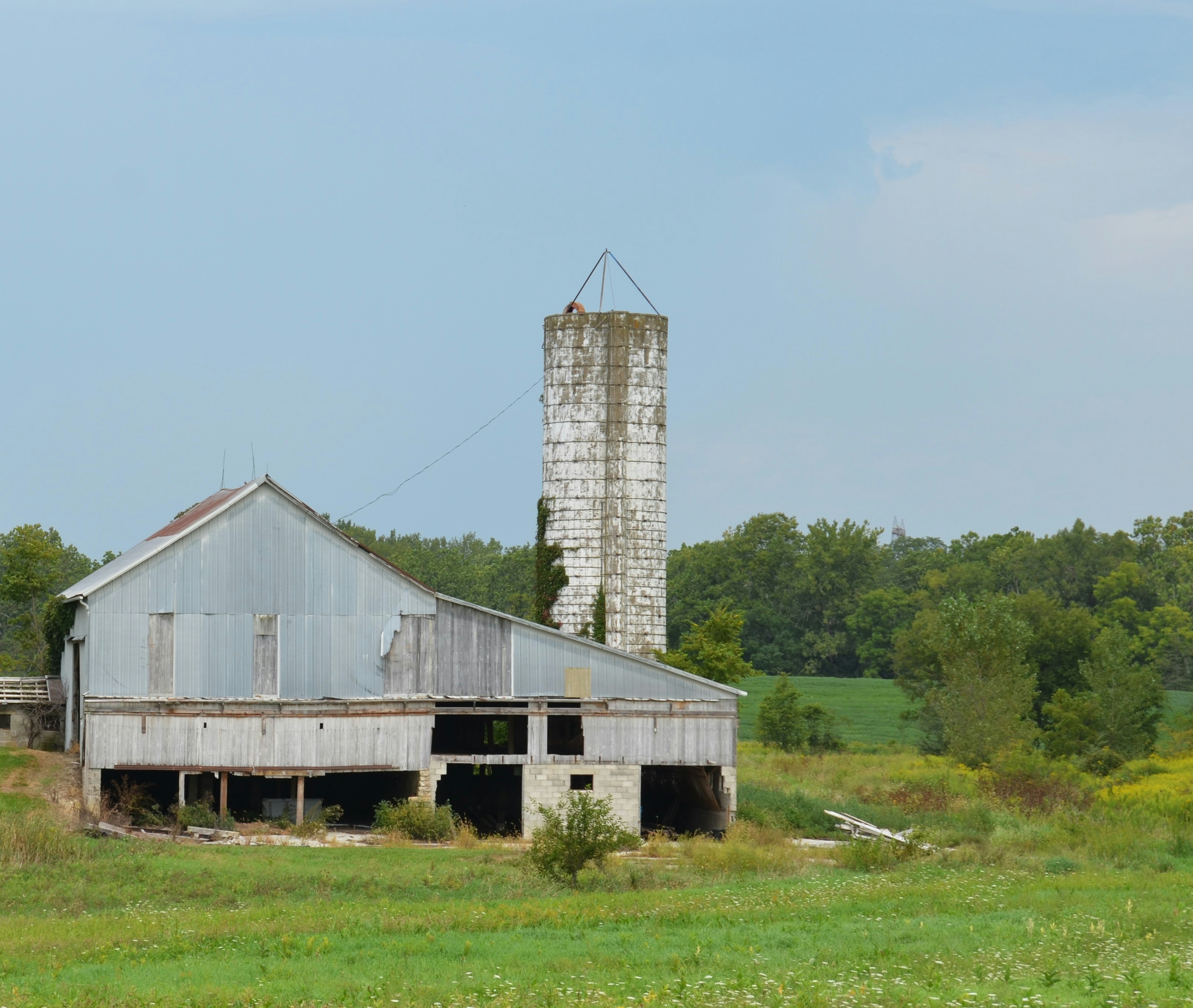 Eine verwitterte Metallscheune und ein hohes Betonsilo auf einem grasbewachsenen Feld