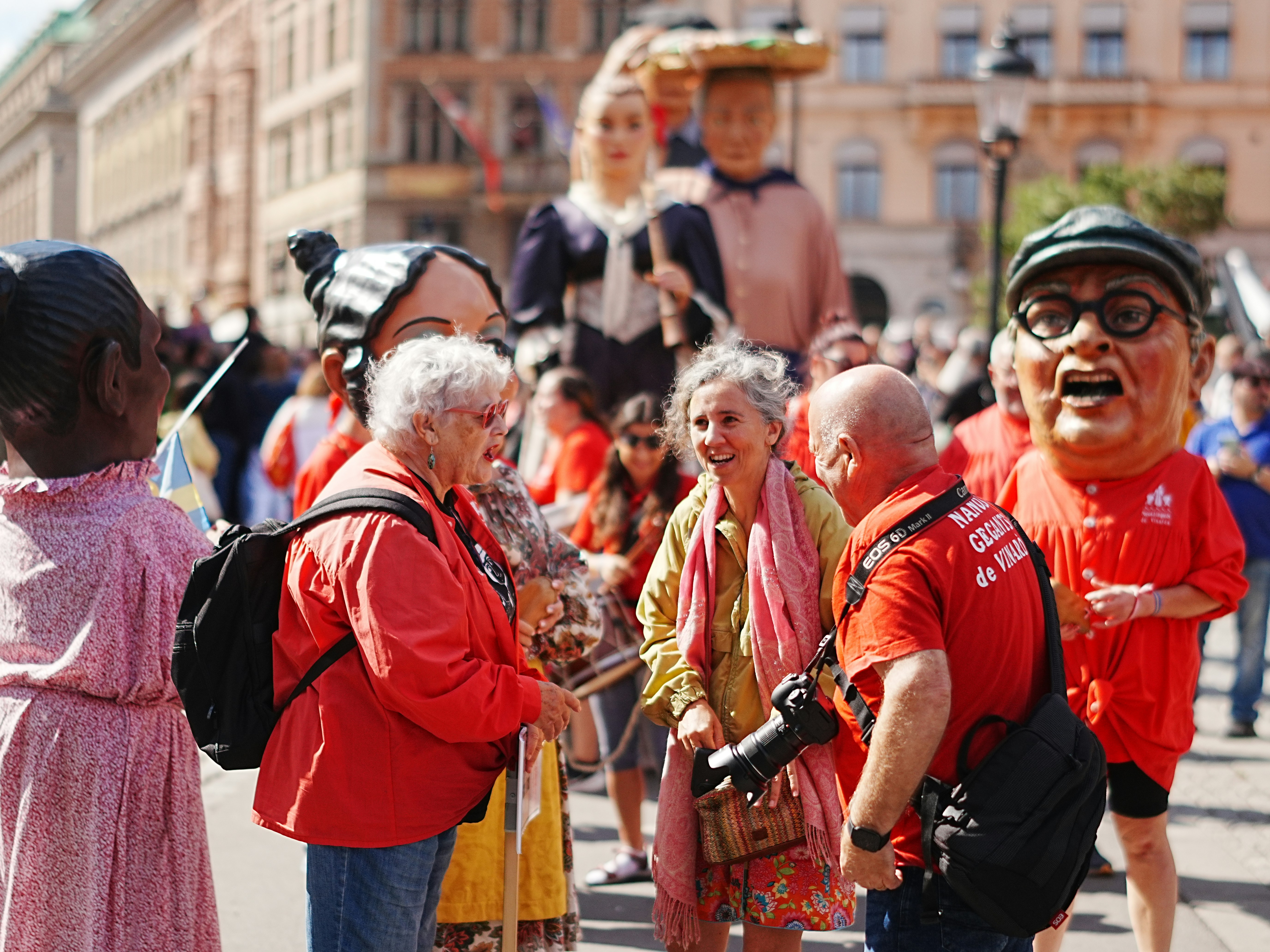People in red shirts talking near large costumed figures in a city square