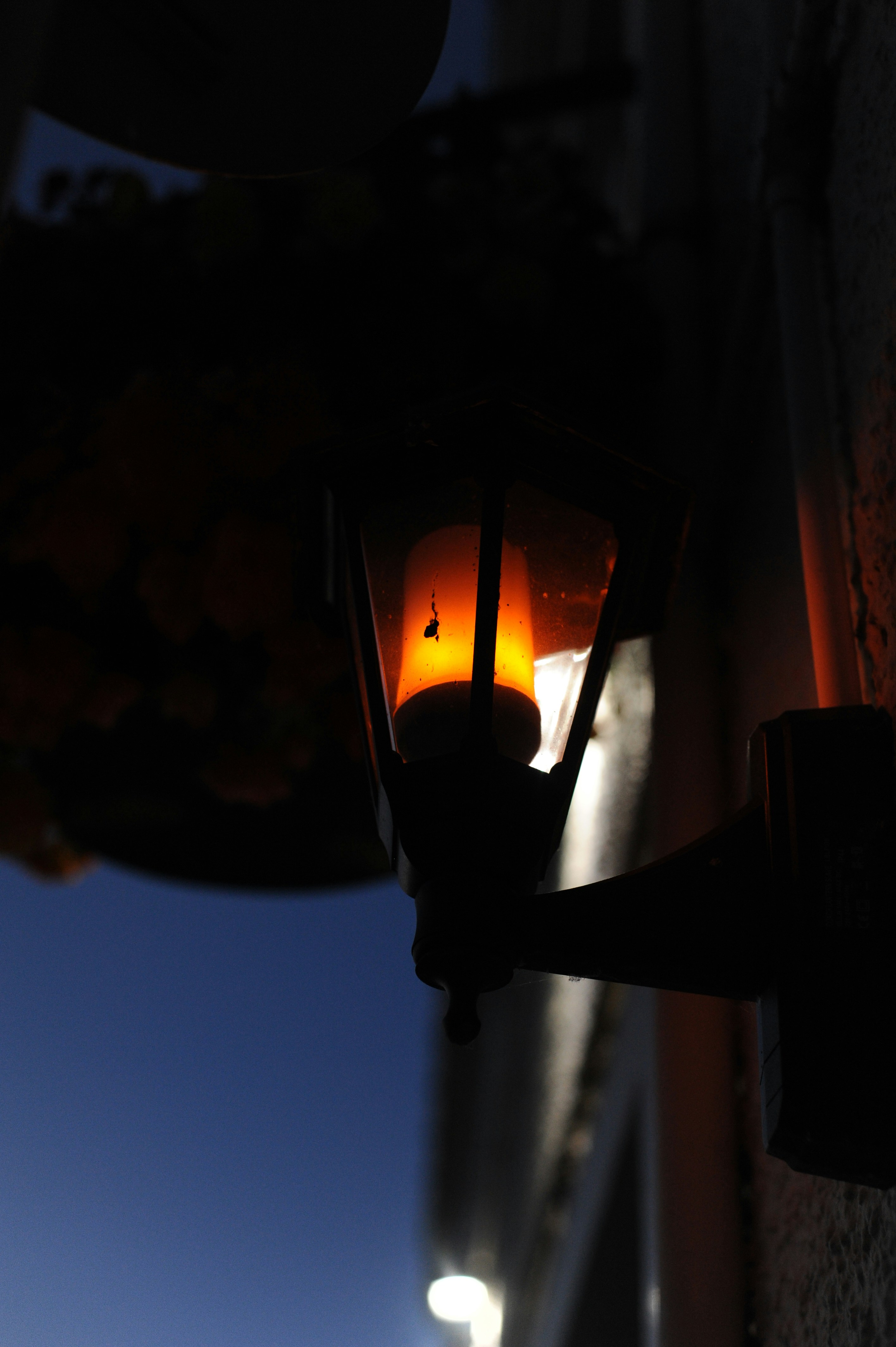 A wall-mounted lantern with a glowing orange light against a dark blue sky