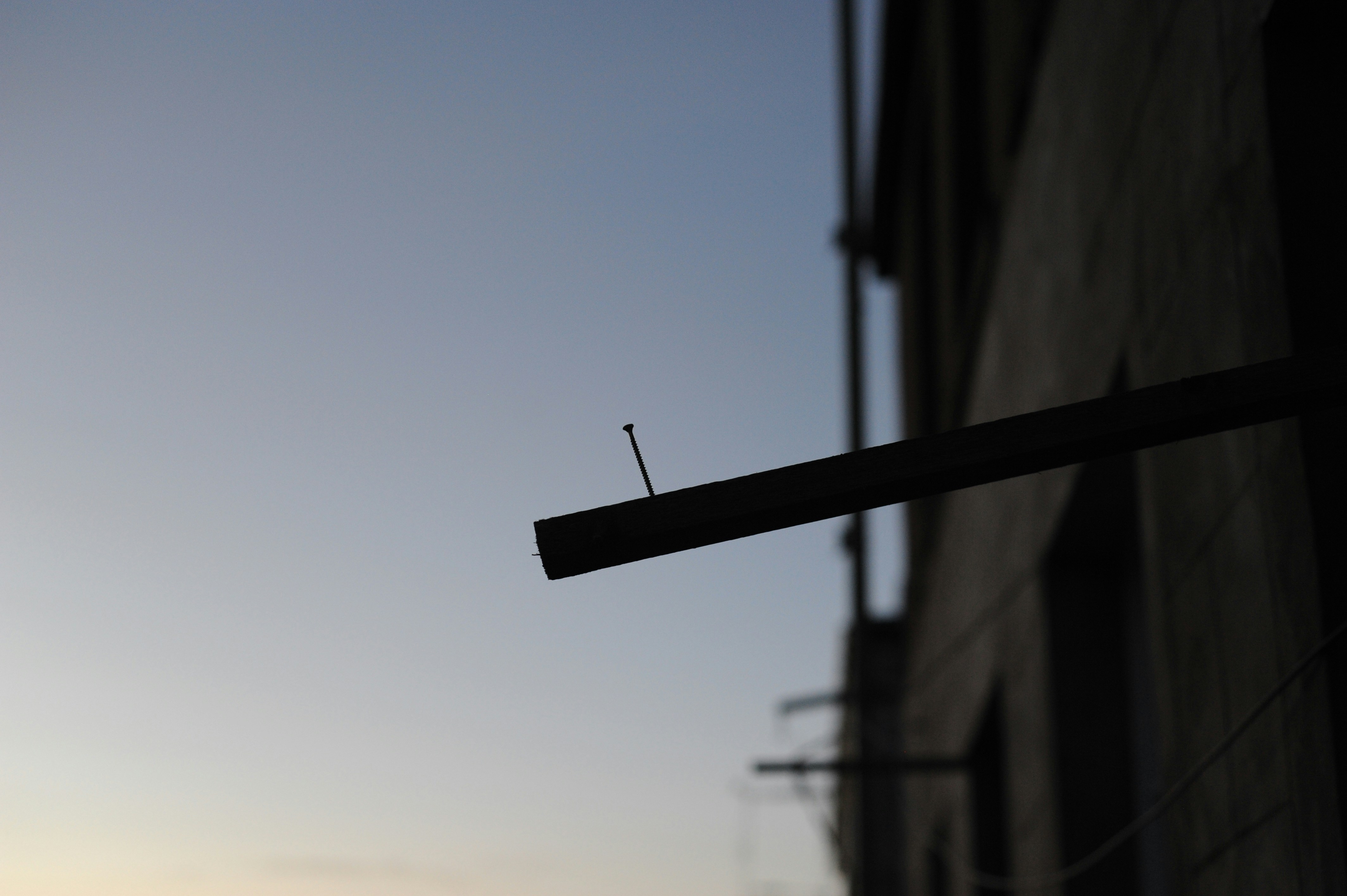 A single nail protruding from a wooden beam against a pale evening sky