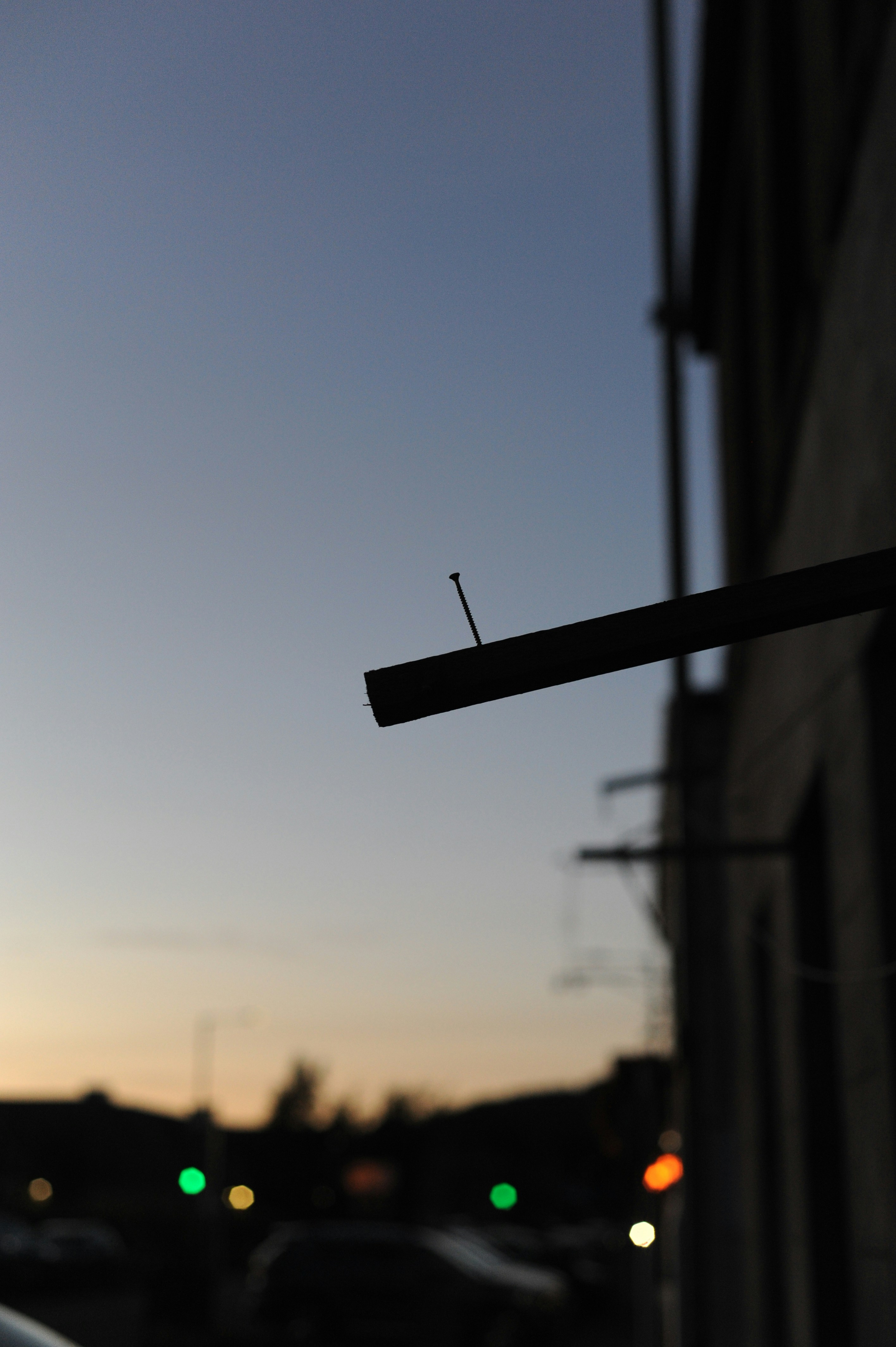 A single nail protruding from a wooden beam against a soft evening sky