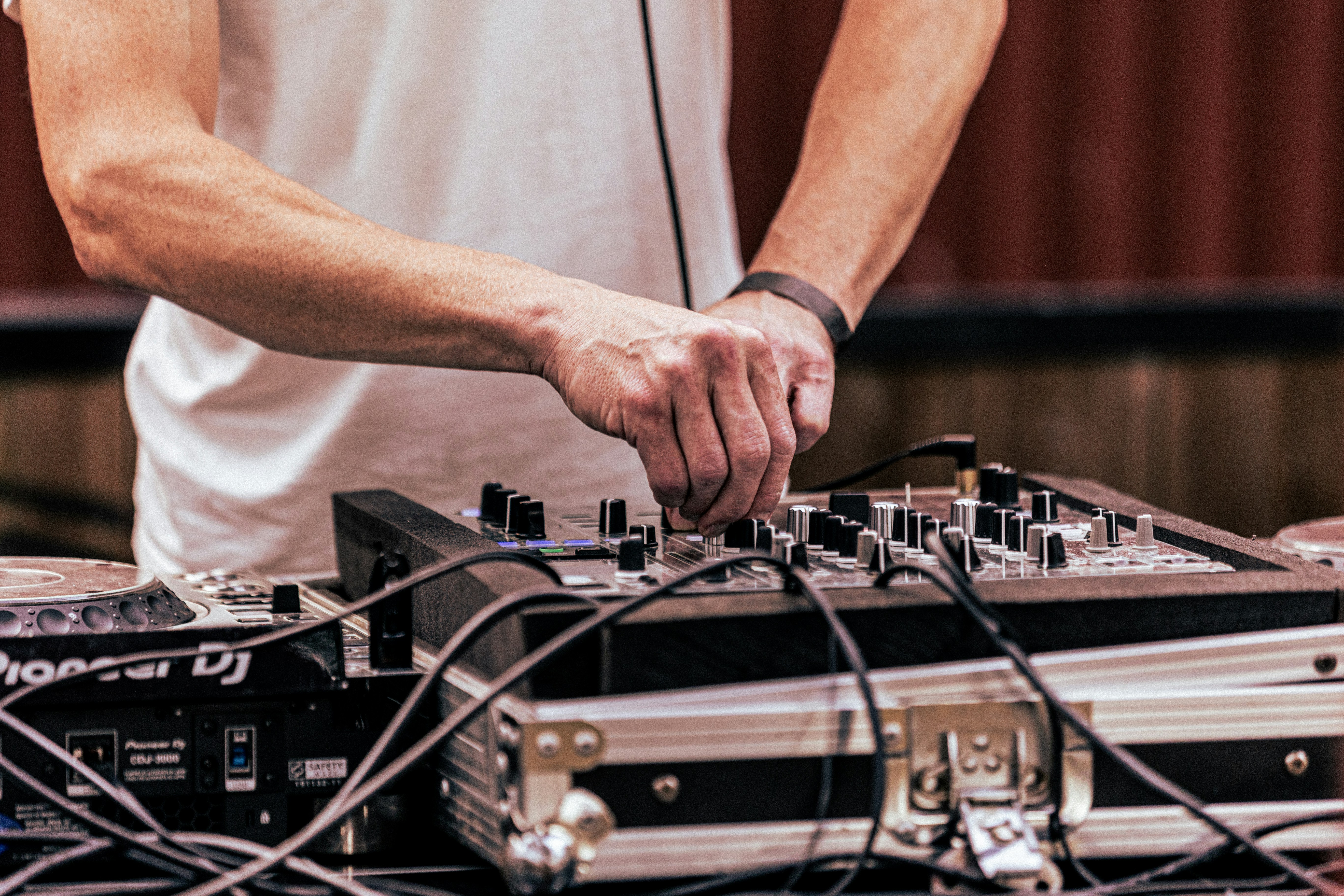 A person in a white t-shirt adjusting knobs on a DJ mixer