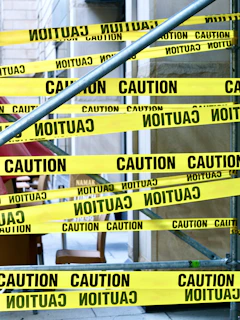 Yellow caution tape wrapped around metal scaffolding in front of a building