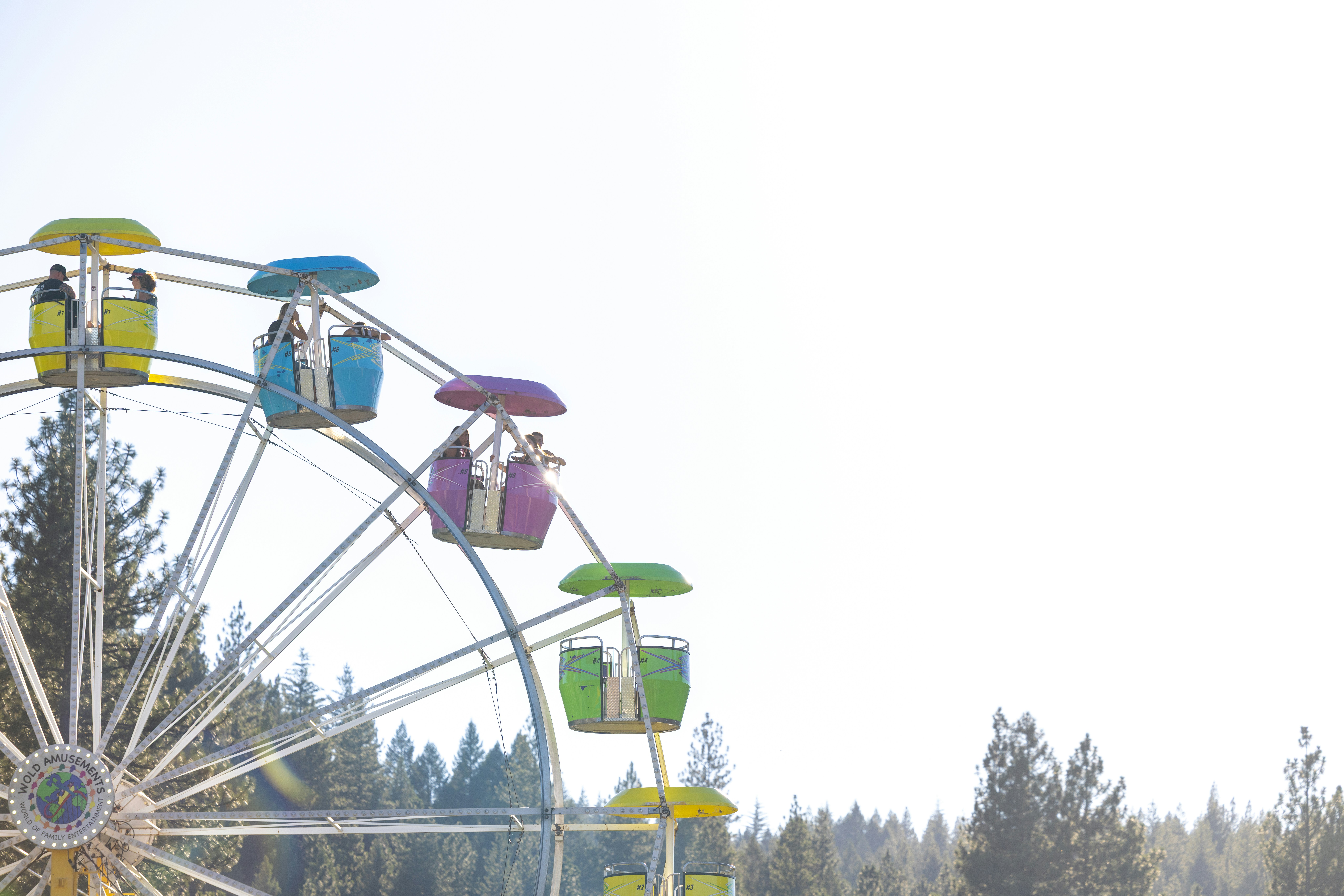 A colorful ferris wheel with people in gondolas against a bright sky and trees