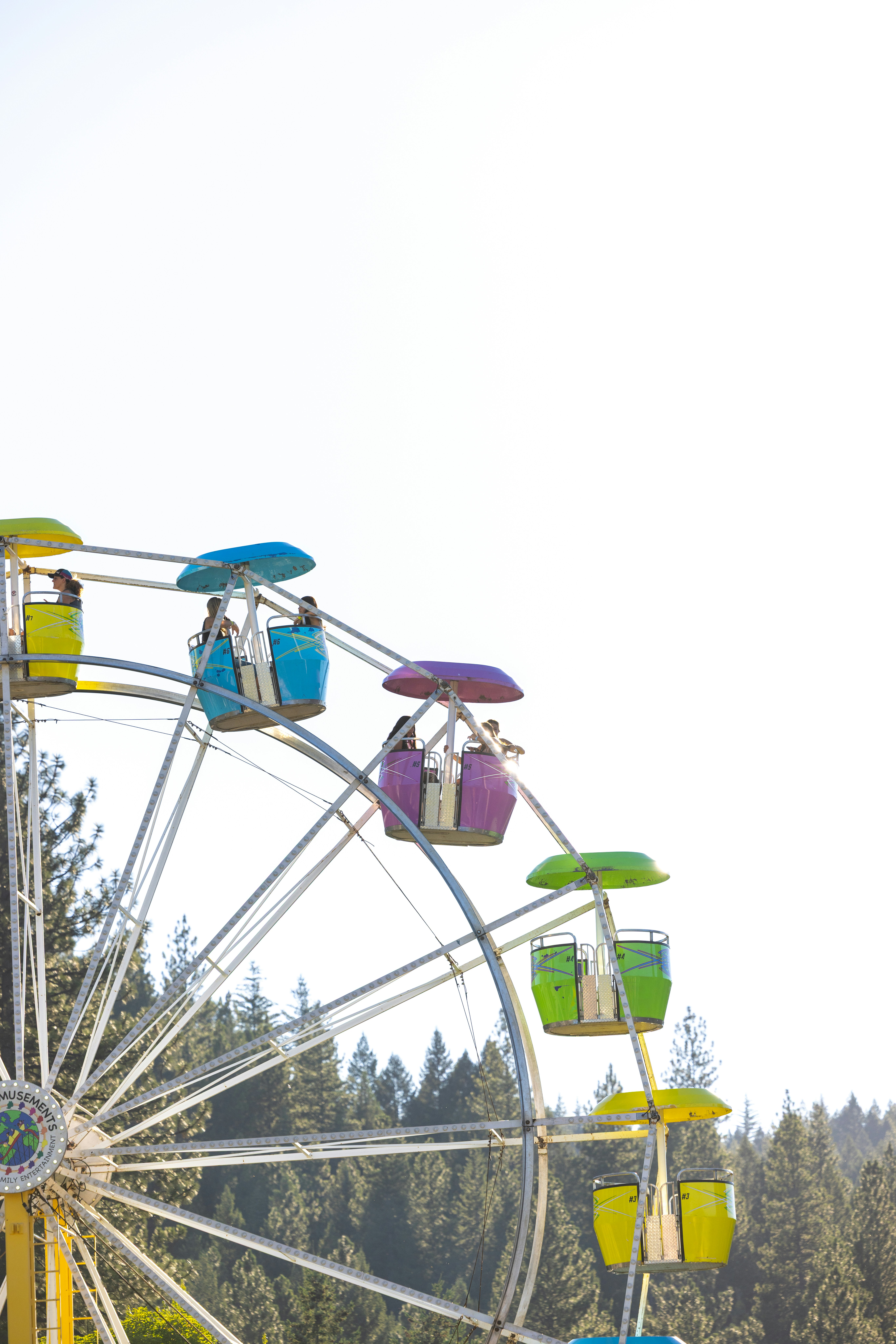 A colorful ferris wheel with people in gondolas against a bright sky and trees