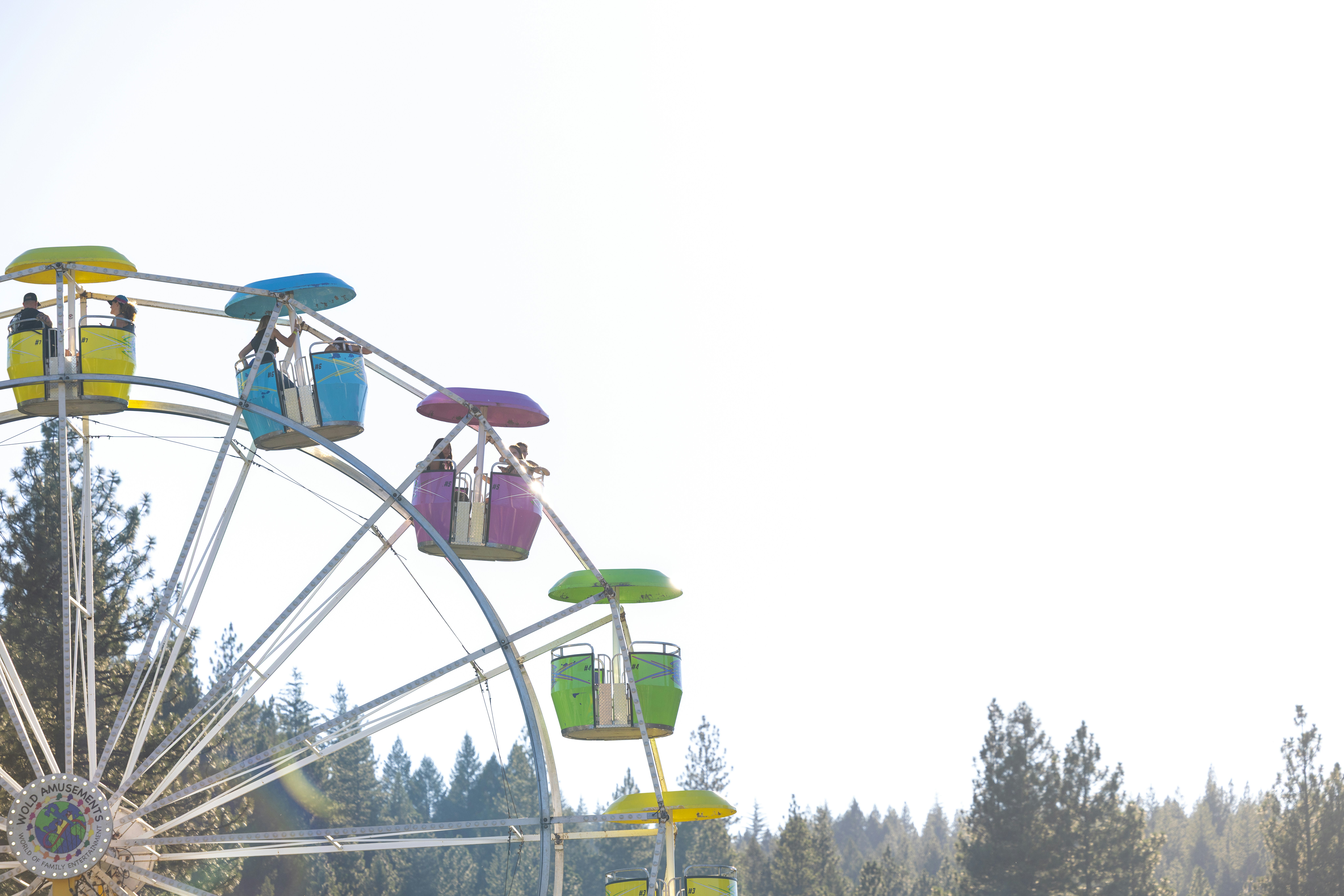 A colorful ferris wheel with people in gondolas against a bright sky and trees