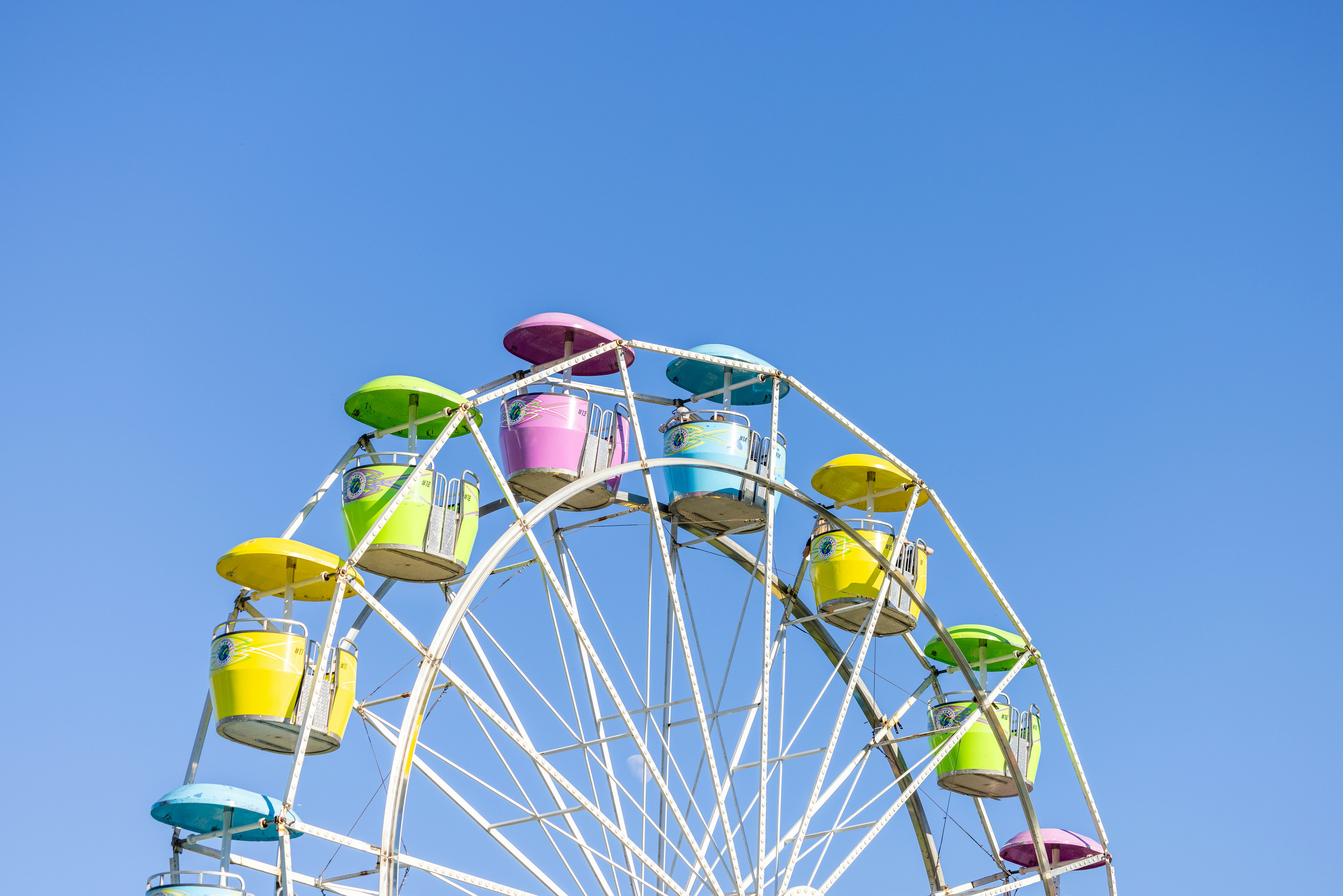 A colorful ferris wheel with bright passenger cars against a clear blue sky