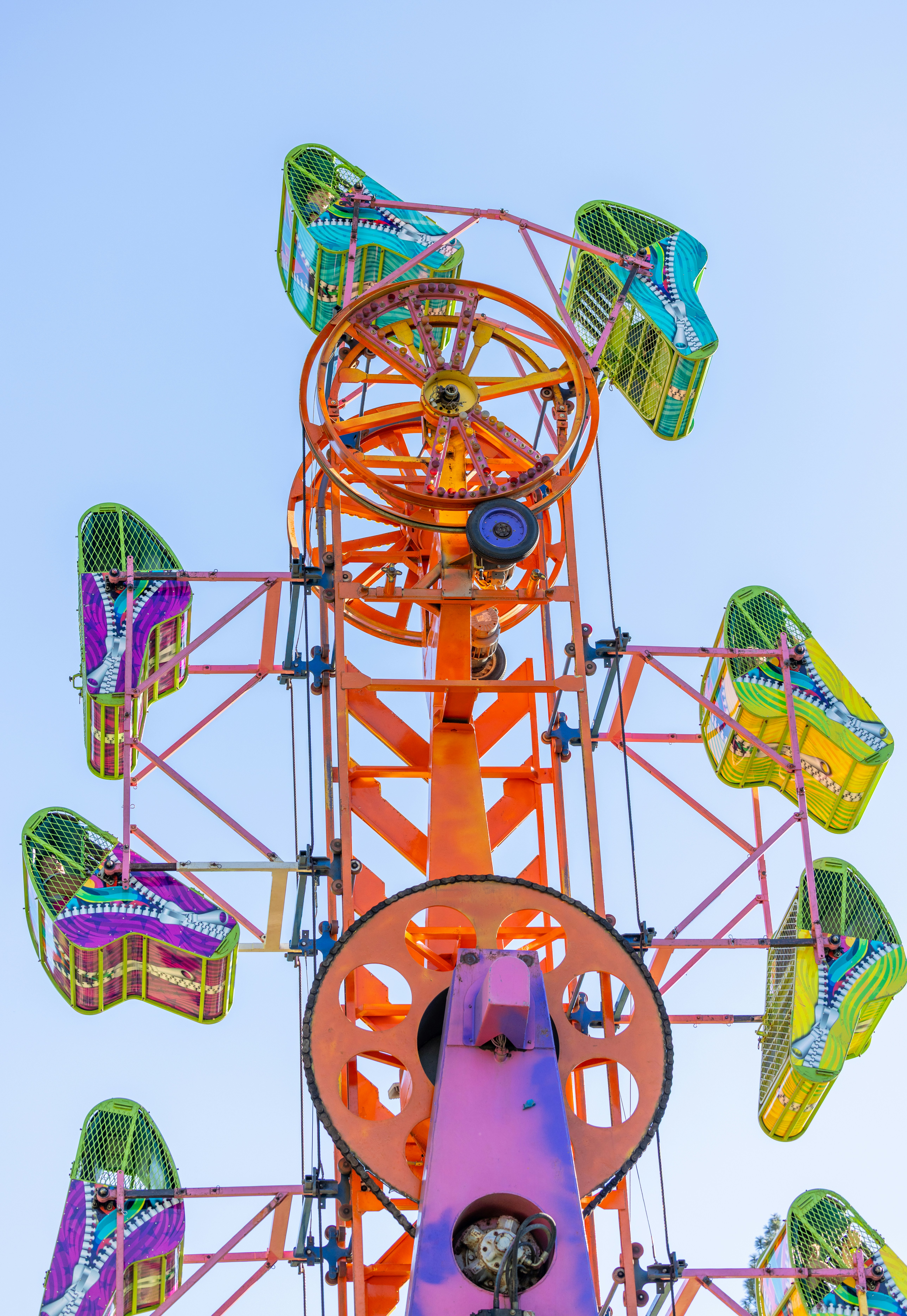 A colorful carnival ride with rotating passenger cars against a clear blue sky