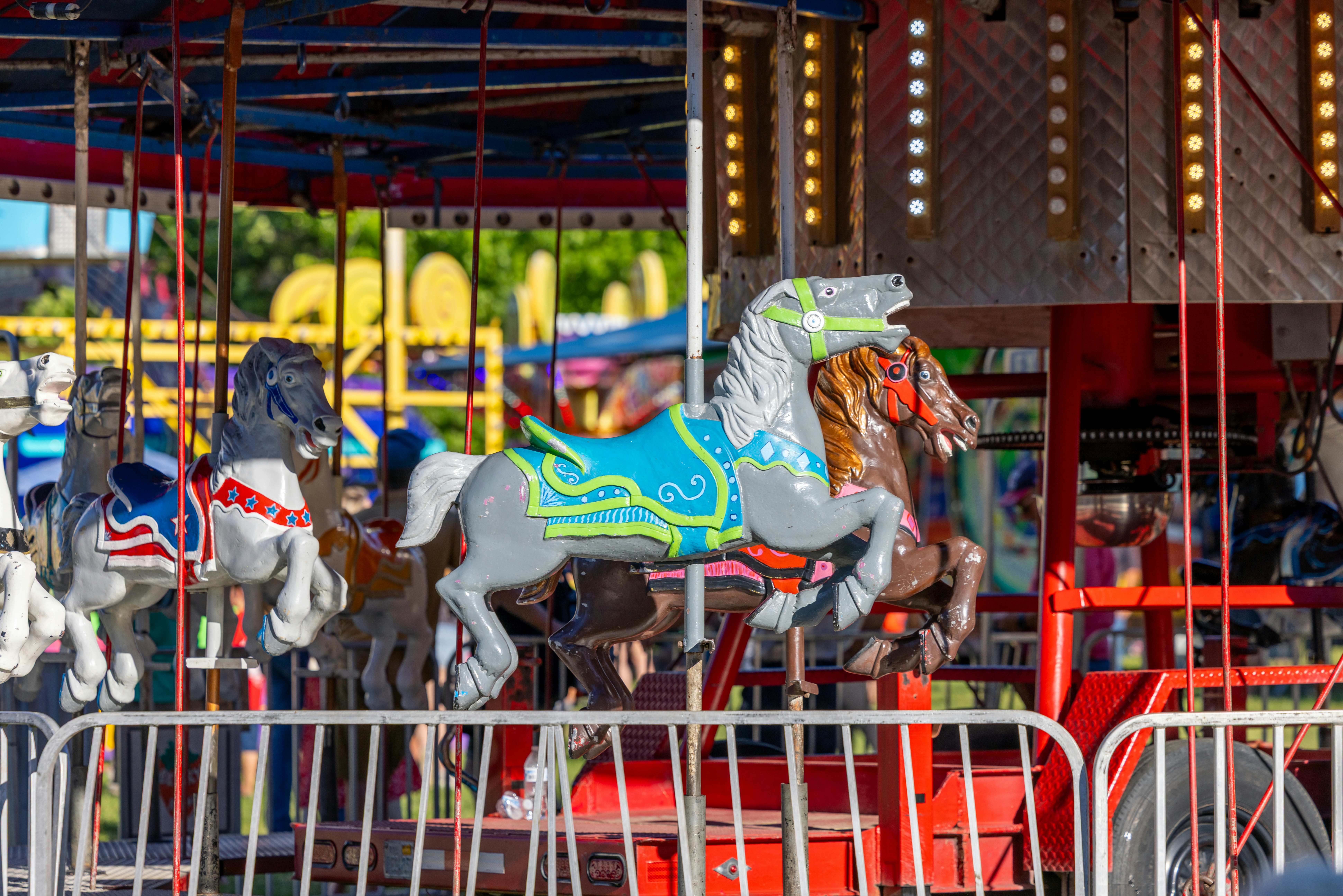 Painted carousel horses on a fairground ride behind a metal safety fence