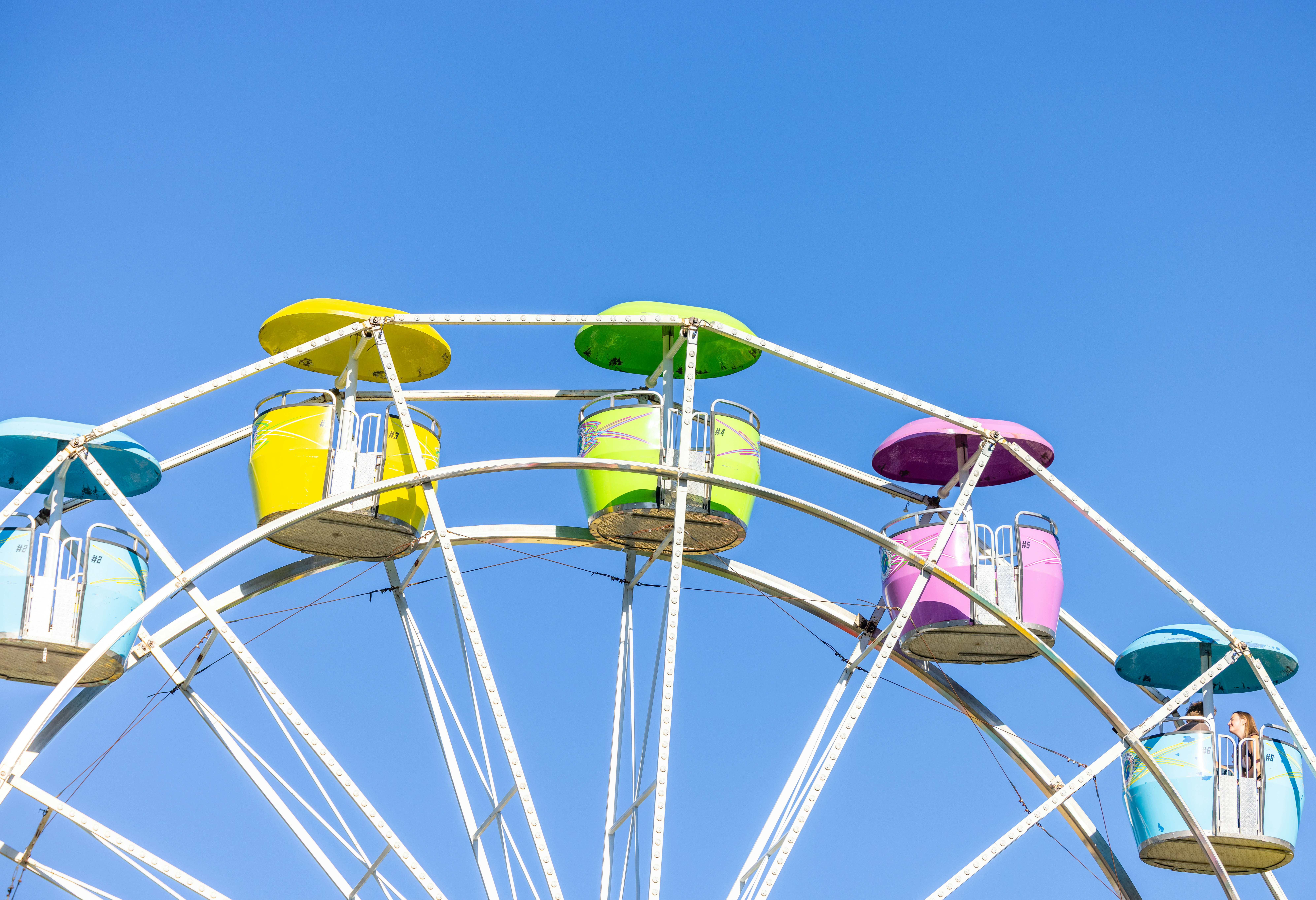 Colorful gondolas on a white ferris wheel against a clear blue sky