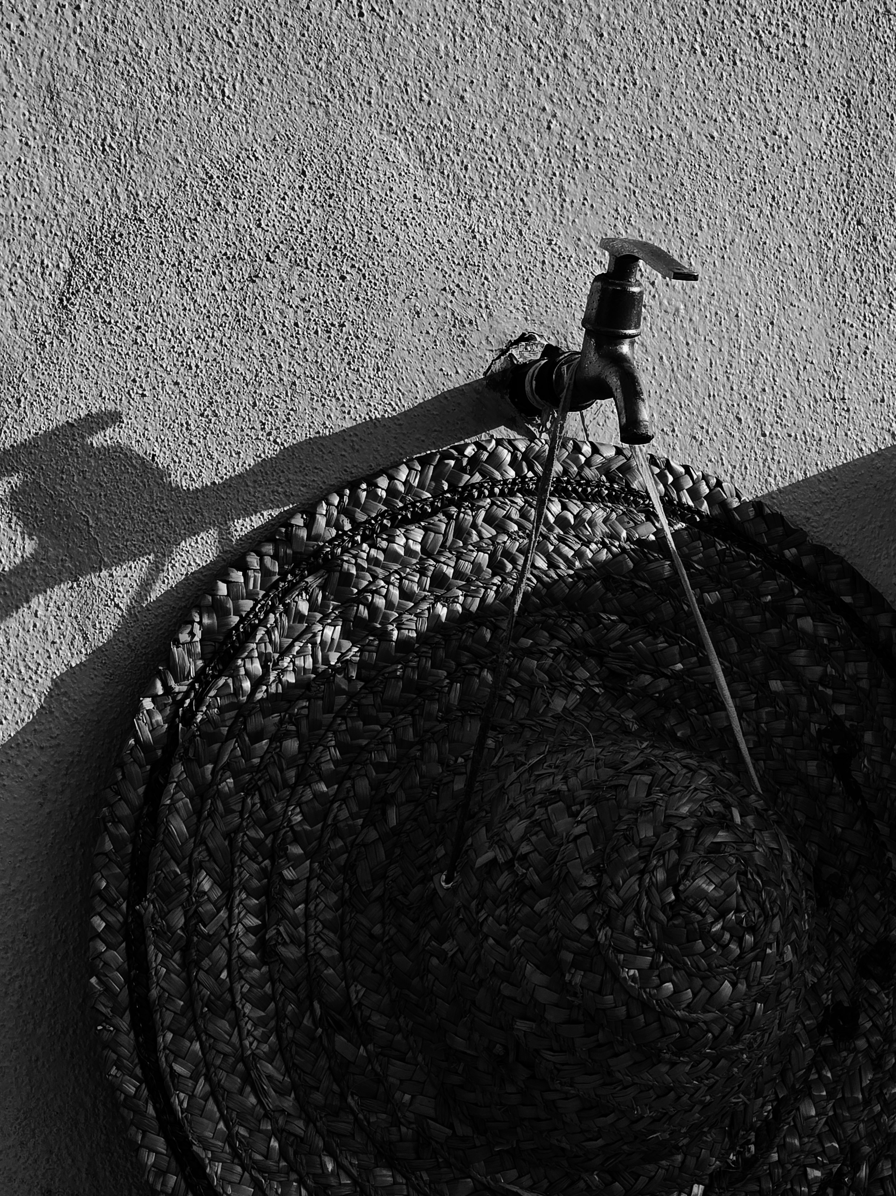 A straw hat hanging on a wall faucet with water flowing from it