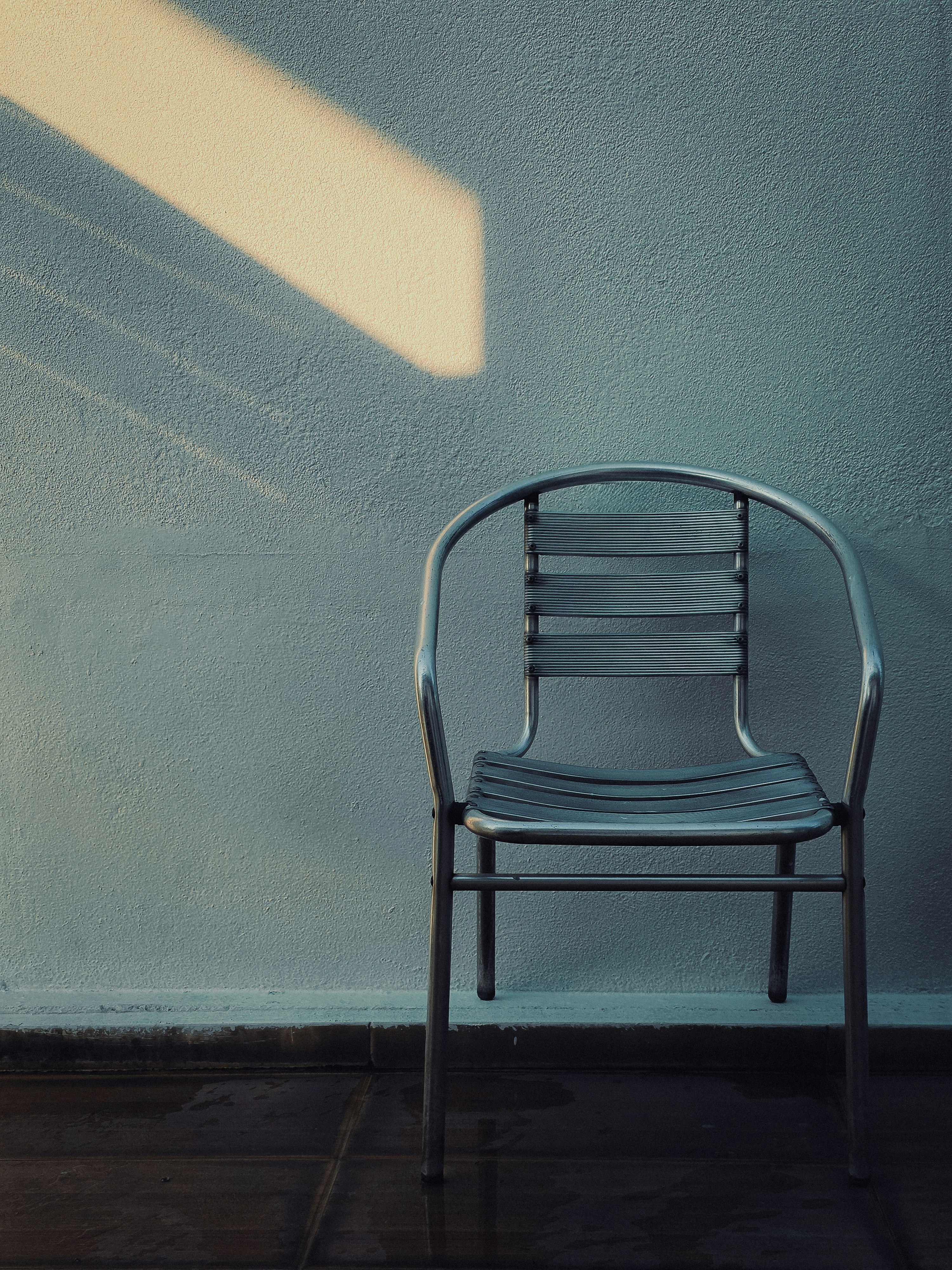 A metal chair against a textured wall with a patch of warm light