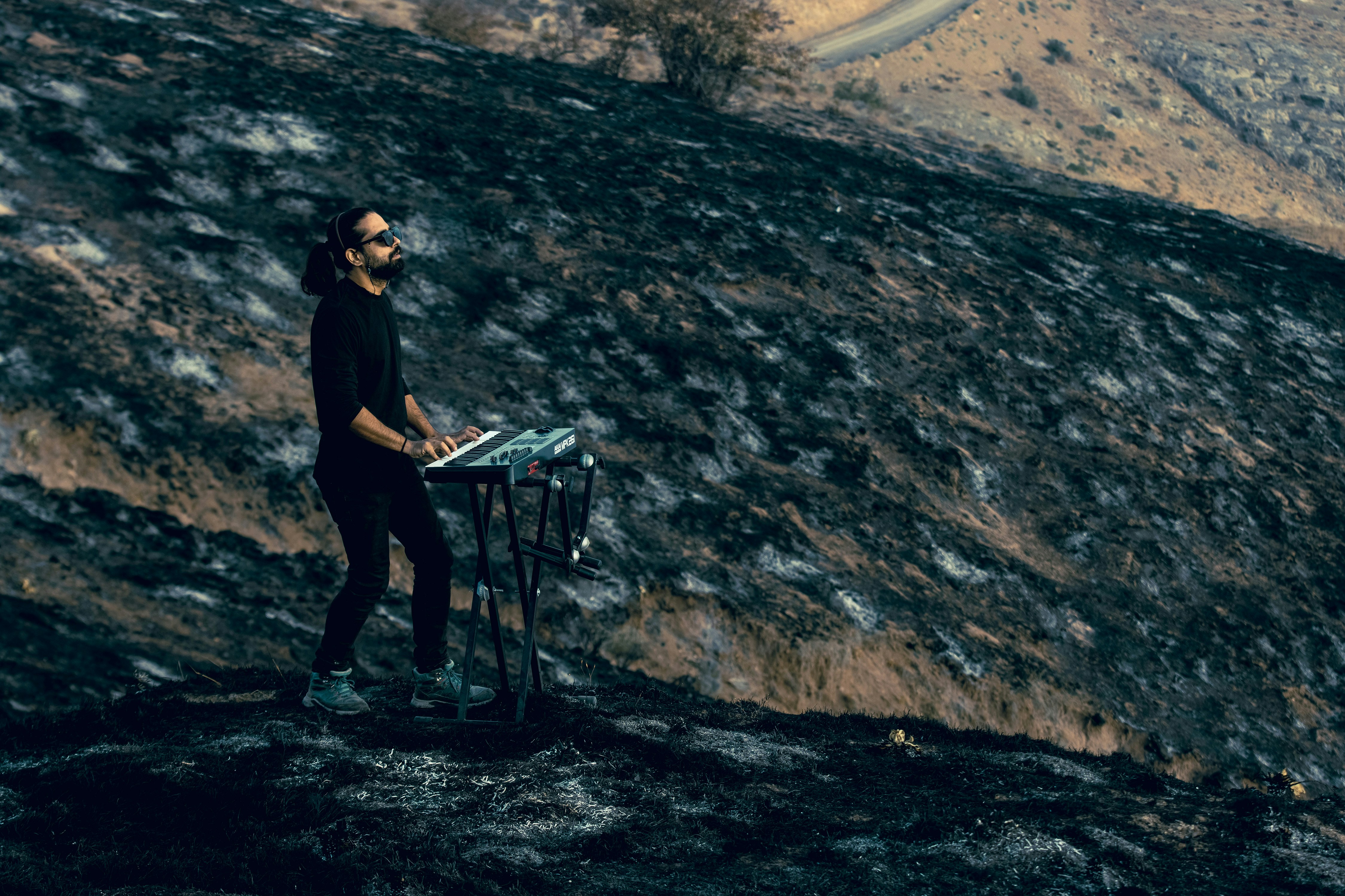 A man playing a keyboard on a charred hillside with dark soil