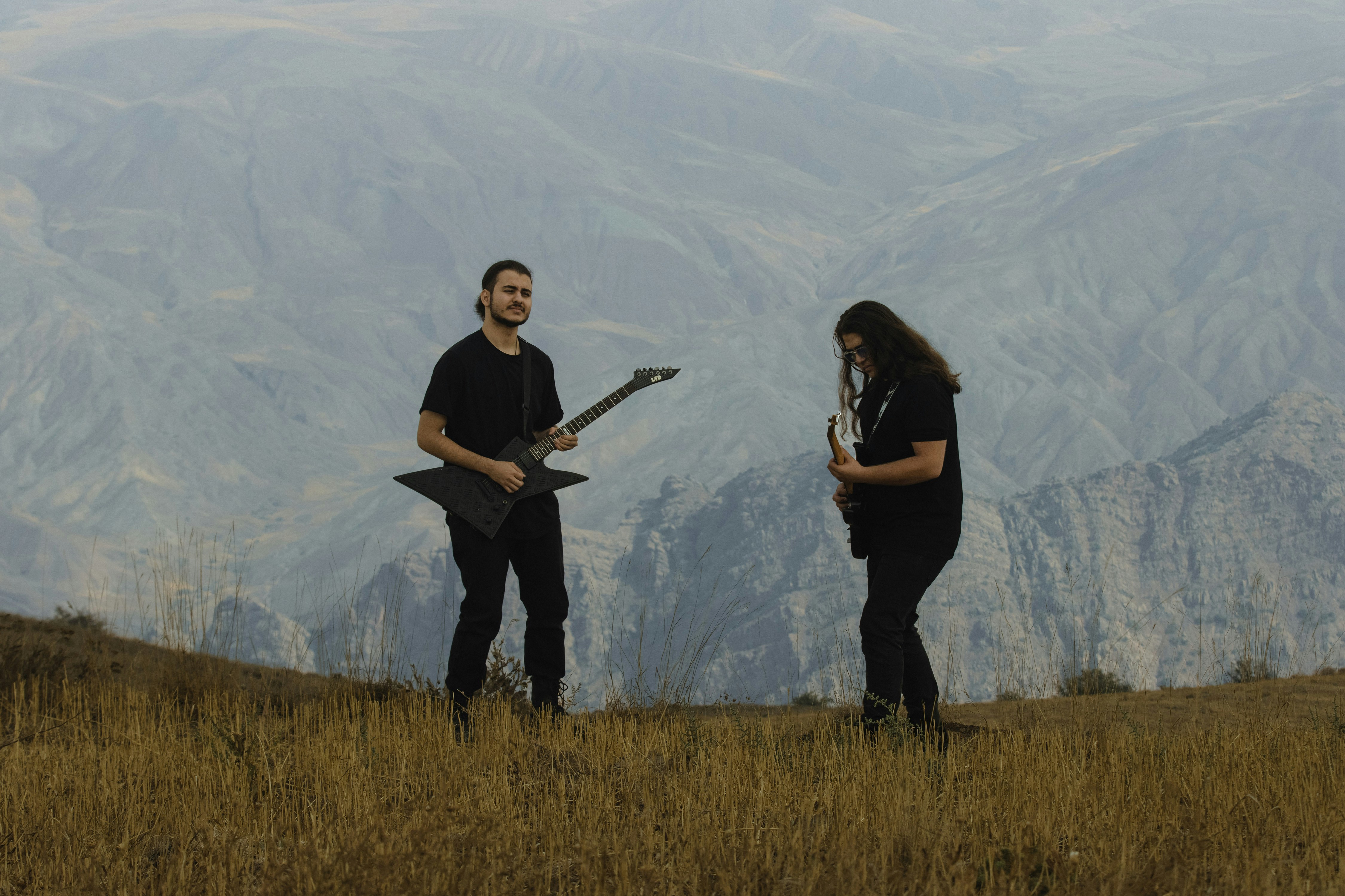 Two people in black clothing playing electric guitars on a dry grassy hillside