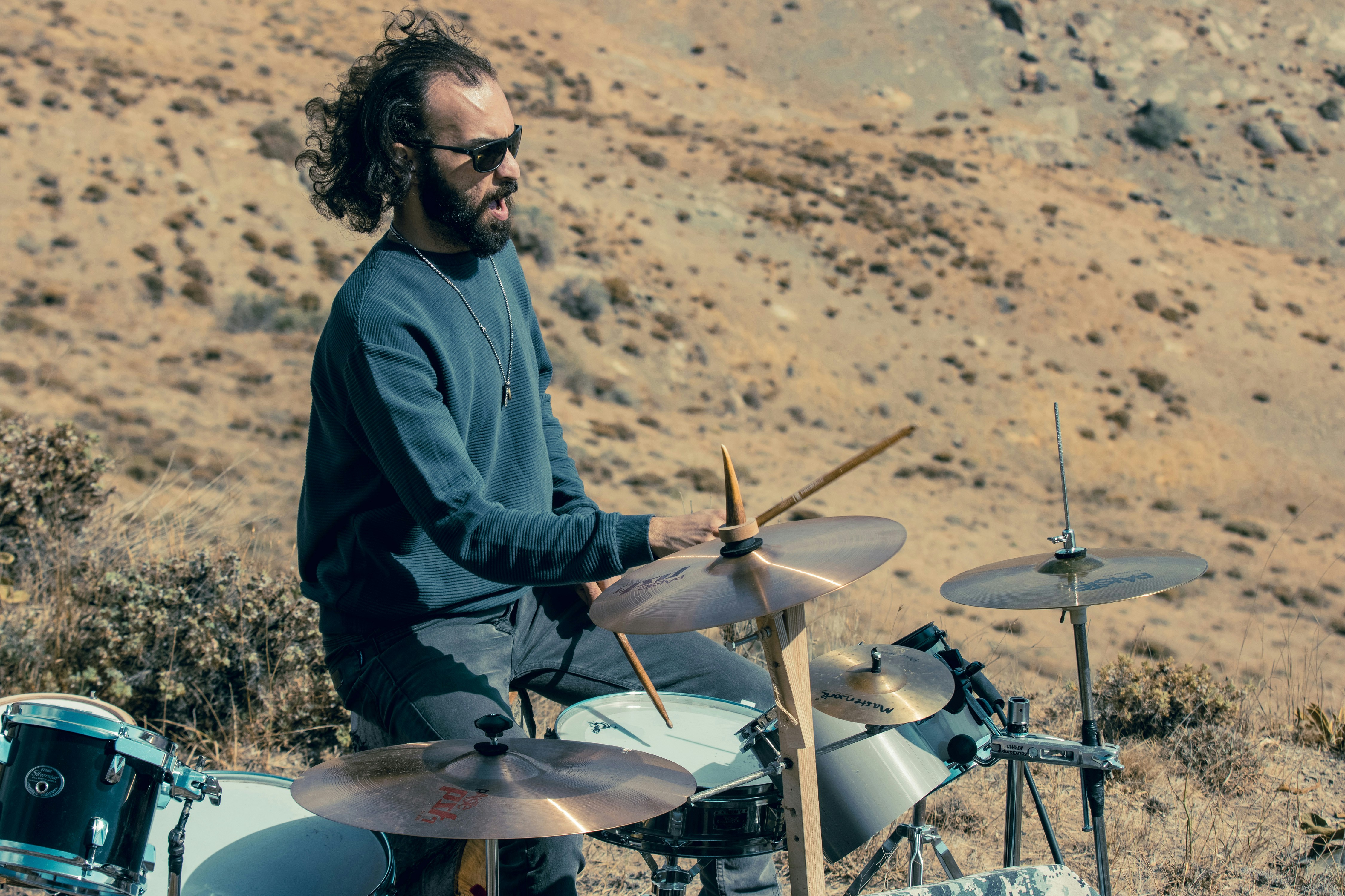 A man with a beard playing drums on a dry, rocky hillside