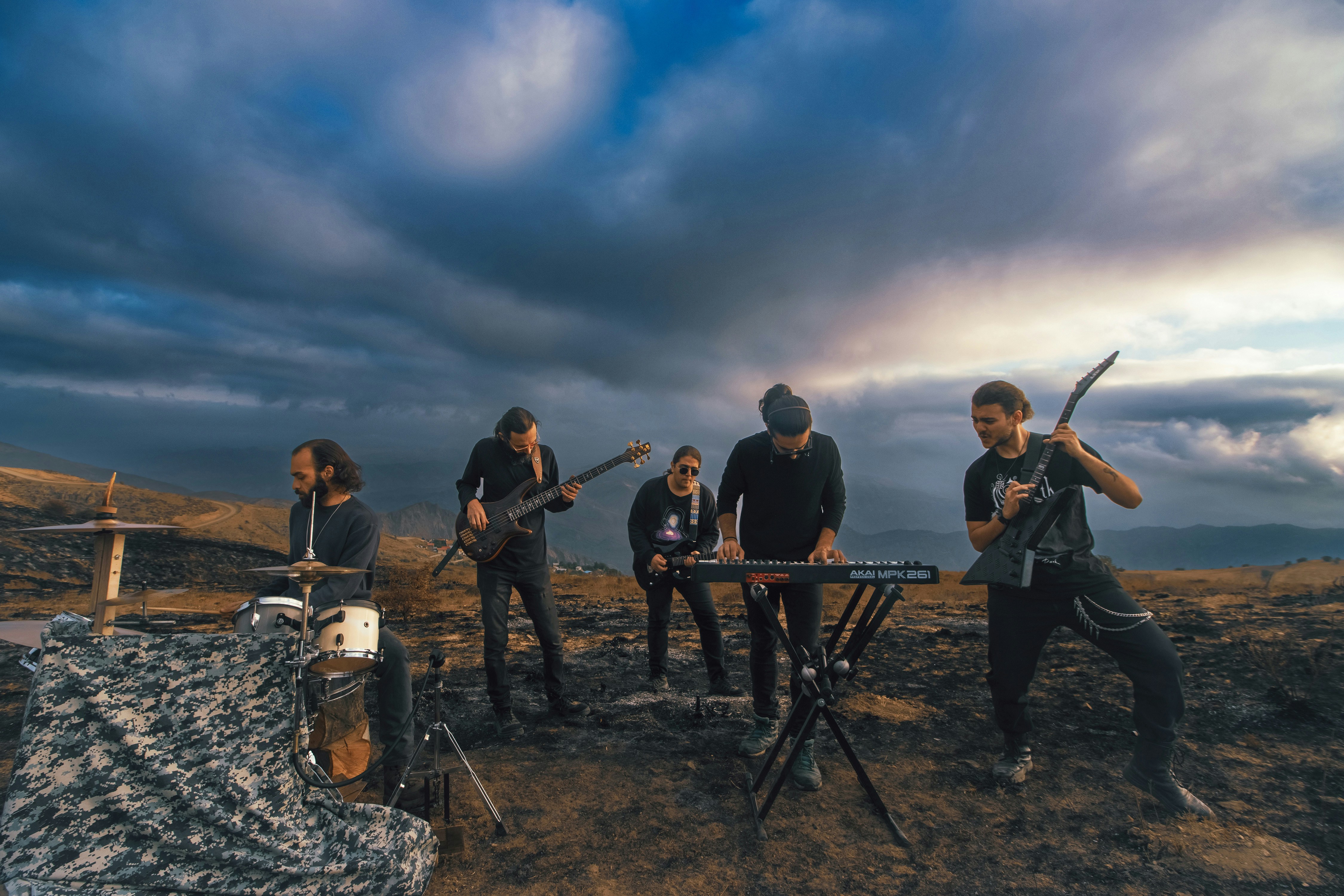 A band playing instruments on a scorched hillside under a dramatic cloudy sky