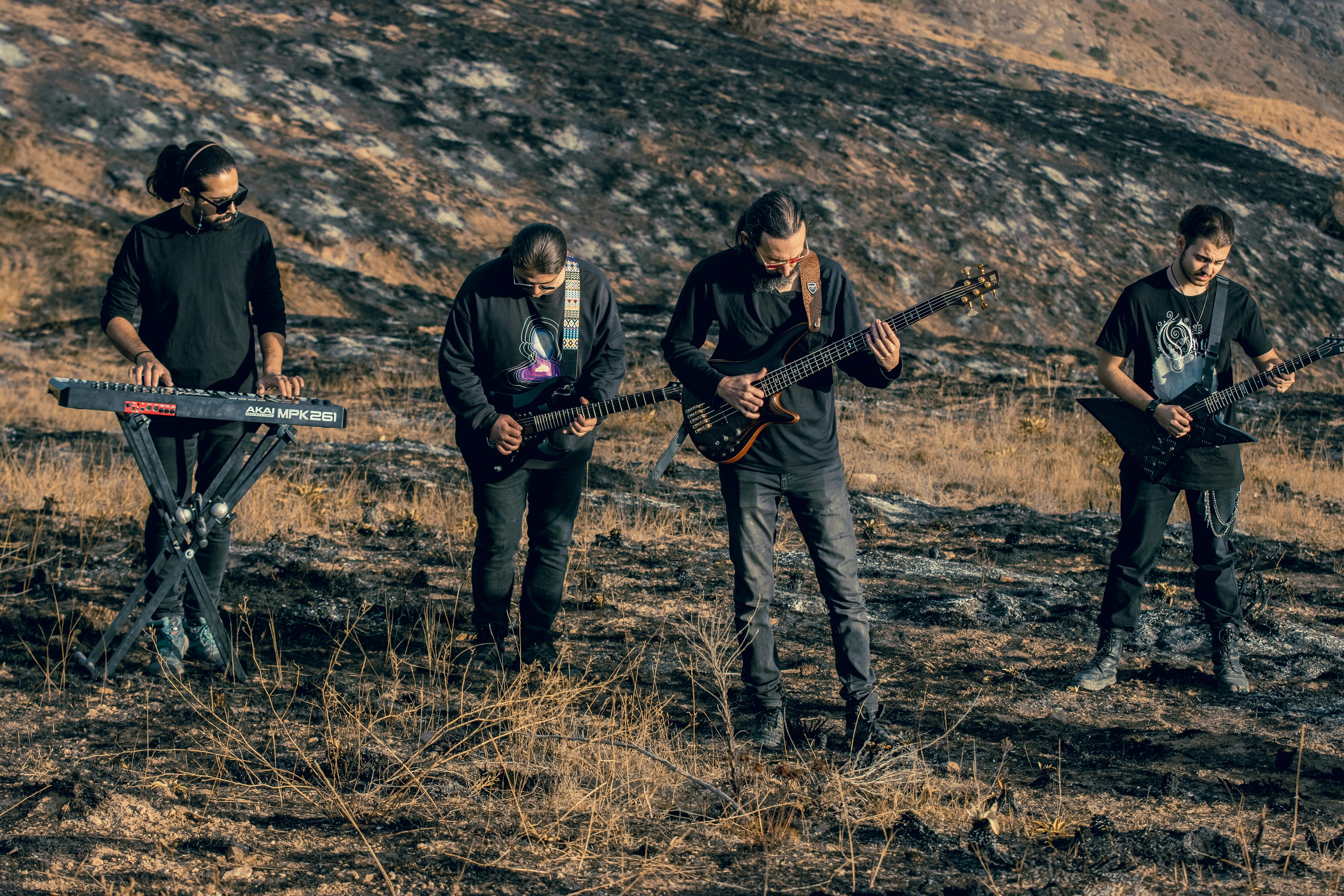 Four musicians playing instruments on a dry, scorched hillside during the golden hour