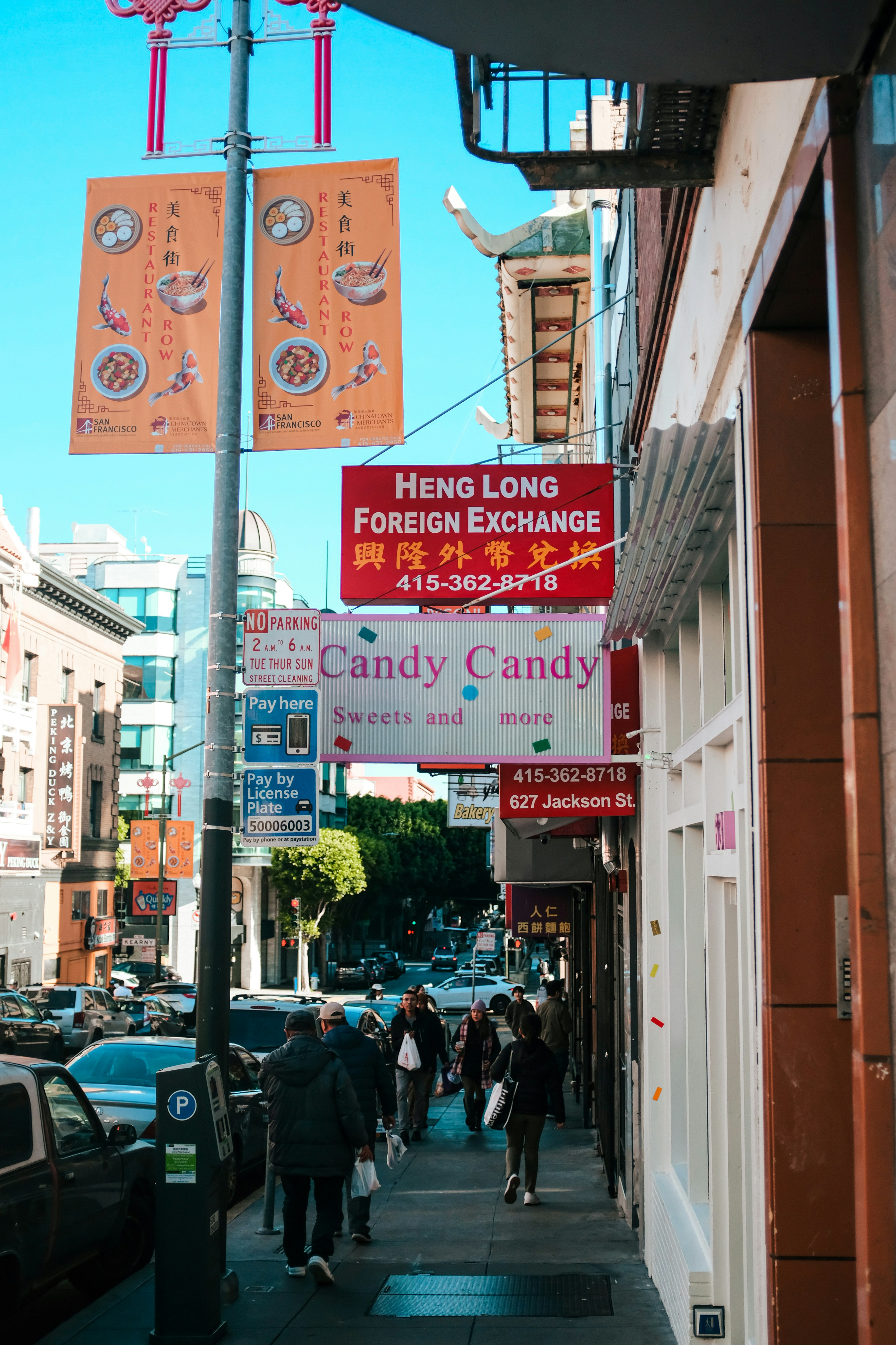 People walking on a sidewalk in Chinatown, San Francisco, past colorful shop signs